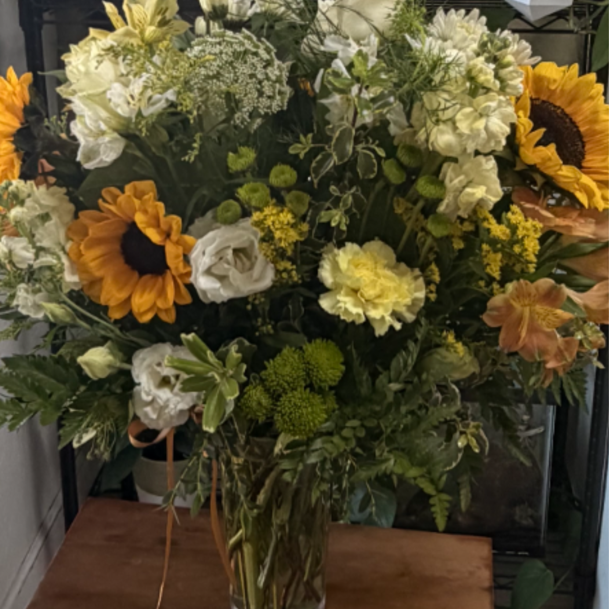 Large mixed bouquet in a clear glass vase with sunflowers and white blooms