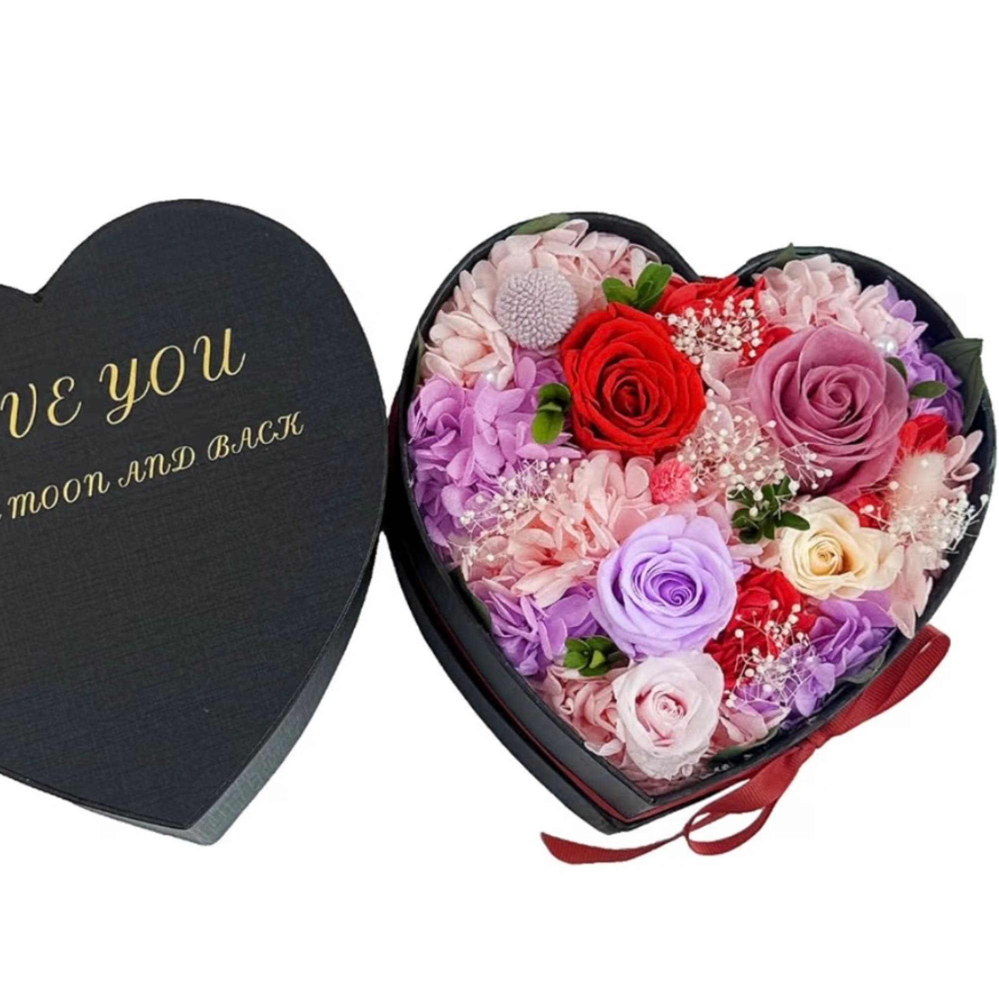 Heart-shaped box of pink and purple roses with a red ribbon