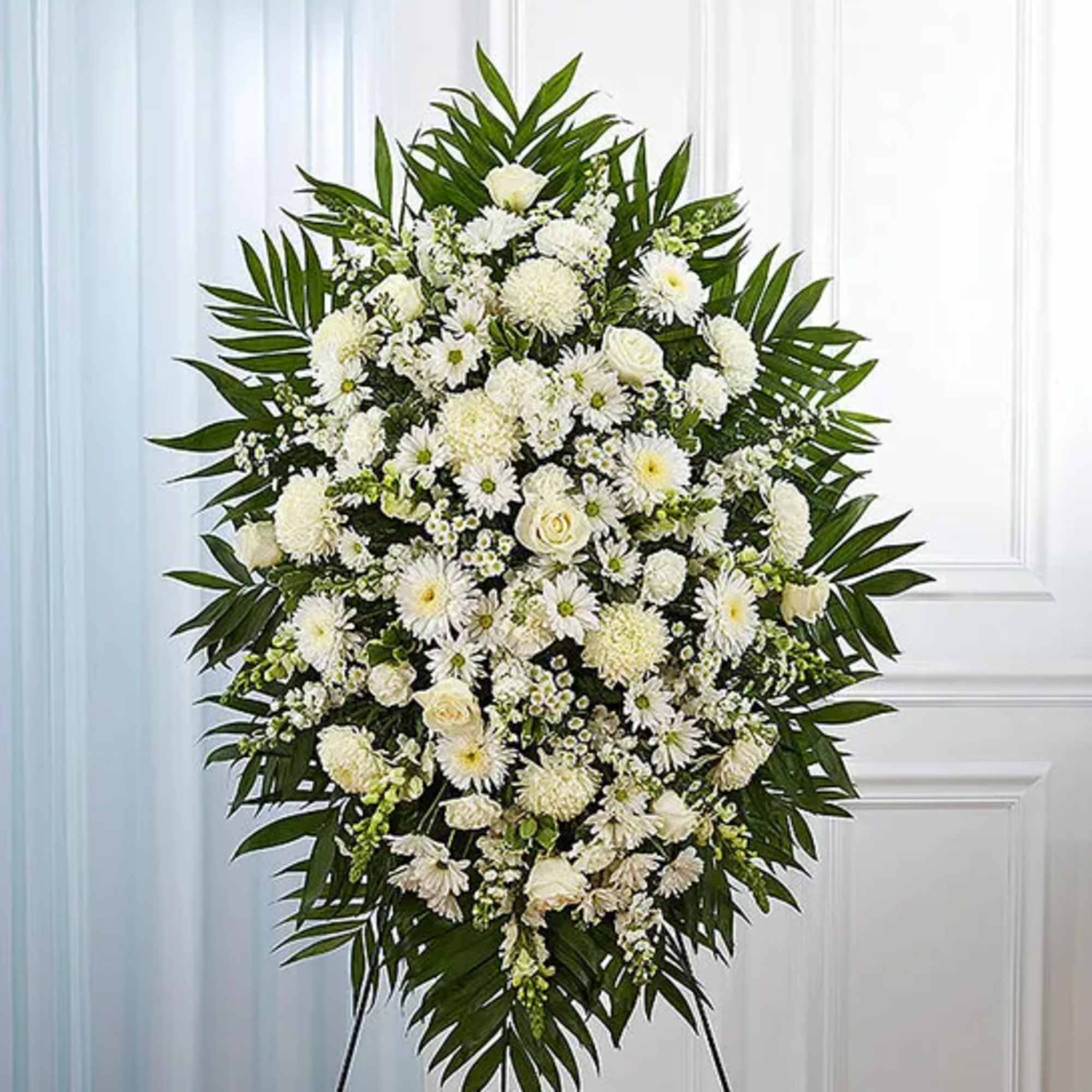 Large white funeral spray with mixed blooms and palm leaves on an easel