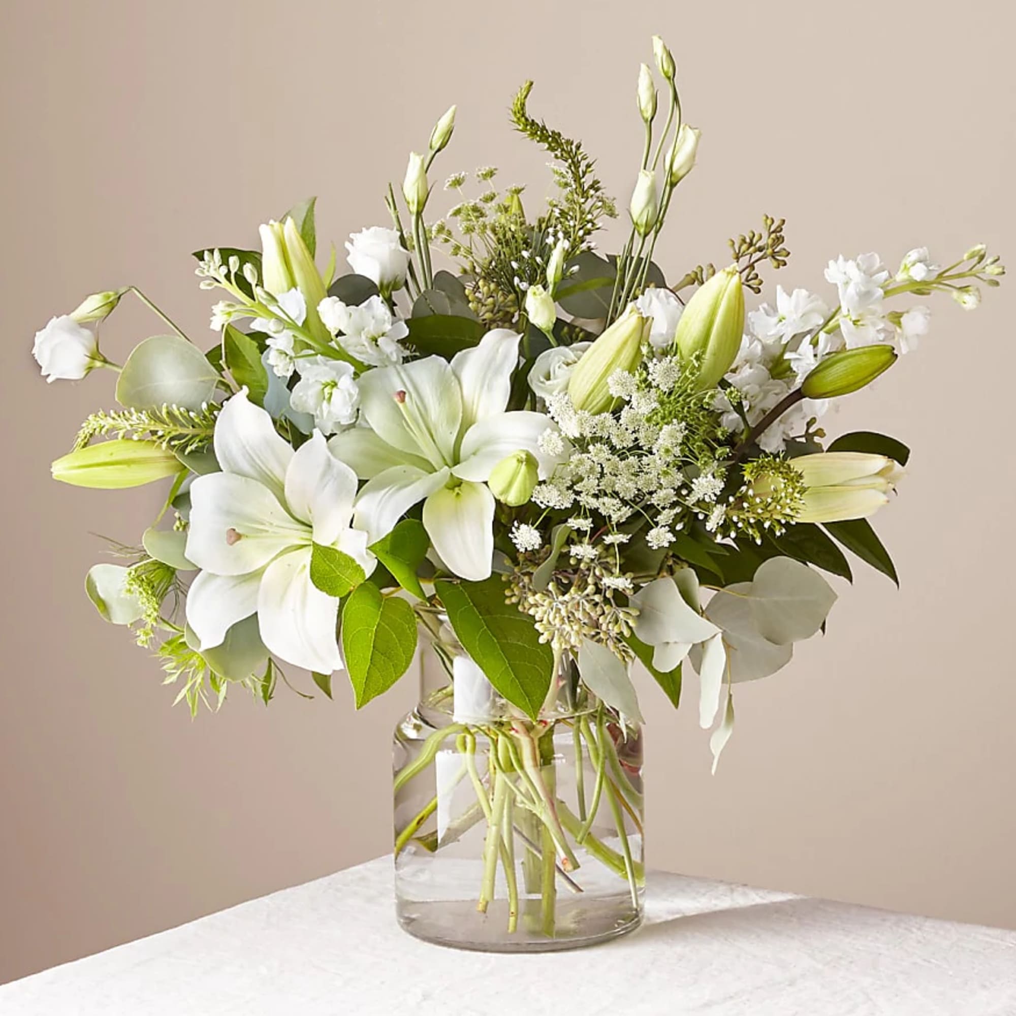 White lilies and small white flowers in a clear glass vase