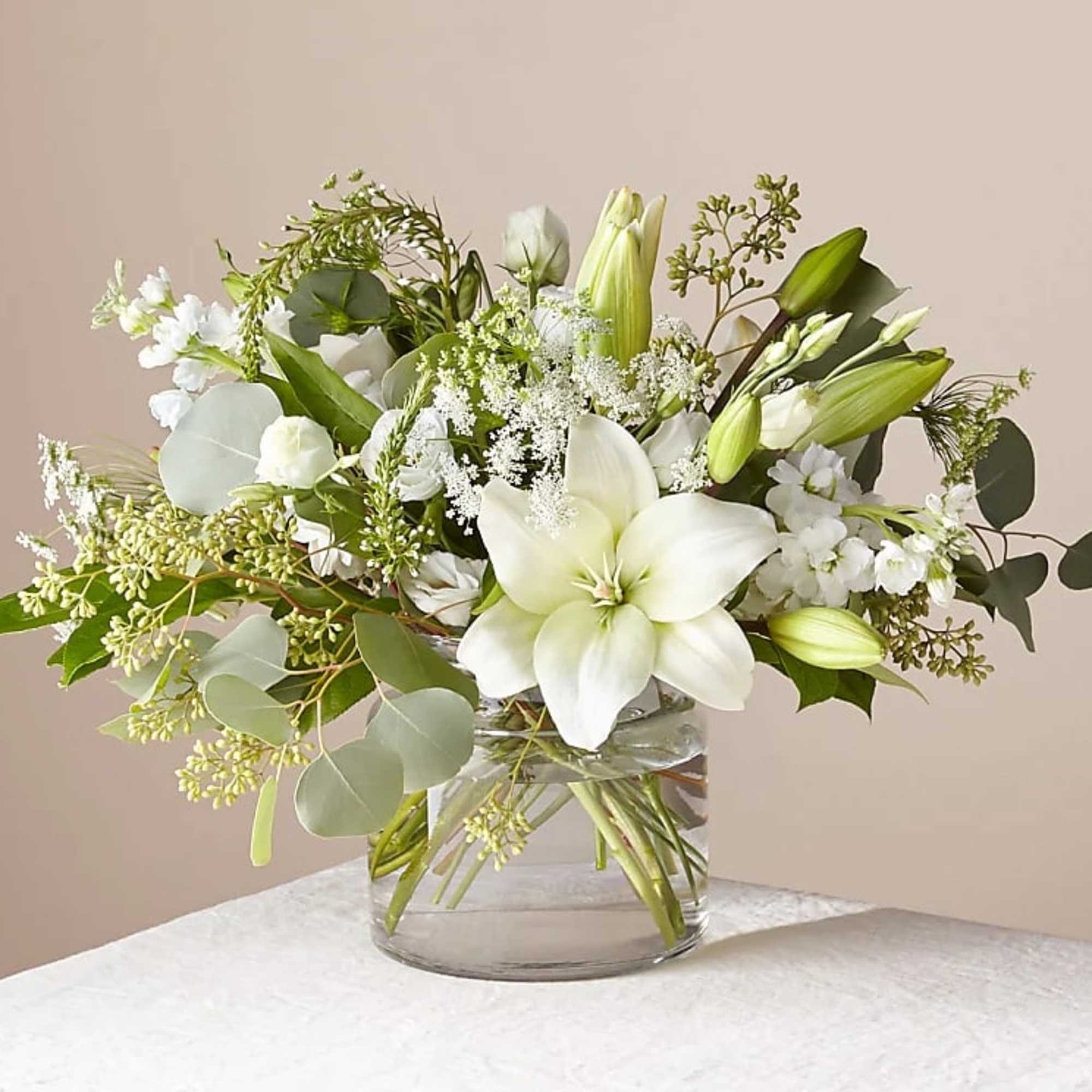 White lilies and small white flowers in a clear glass vase