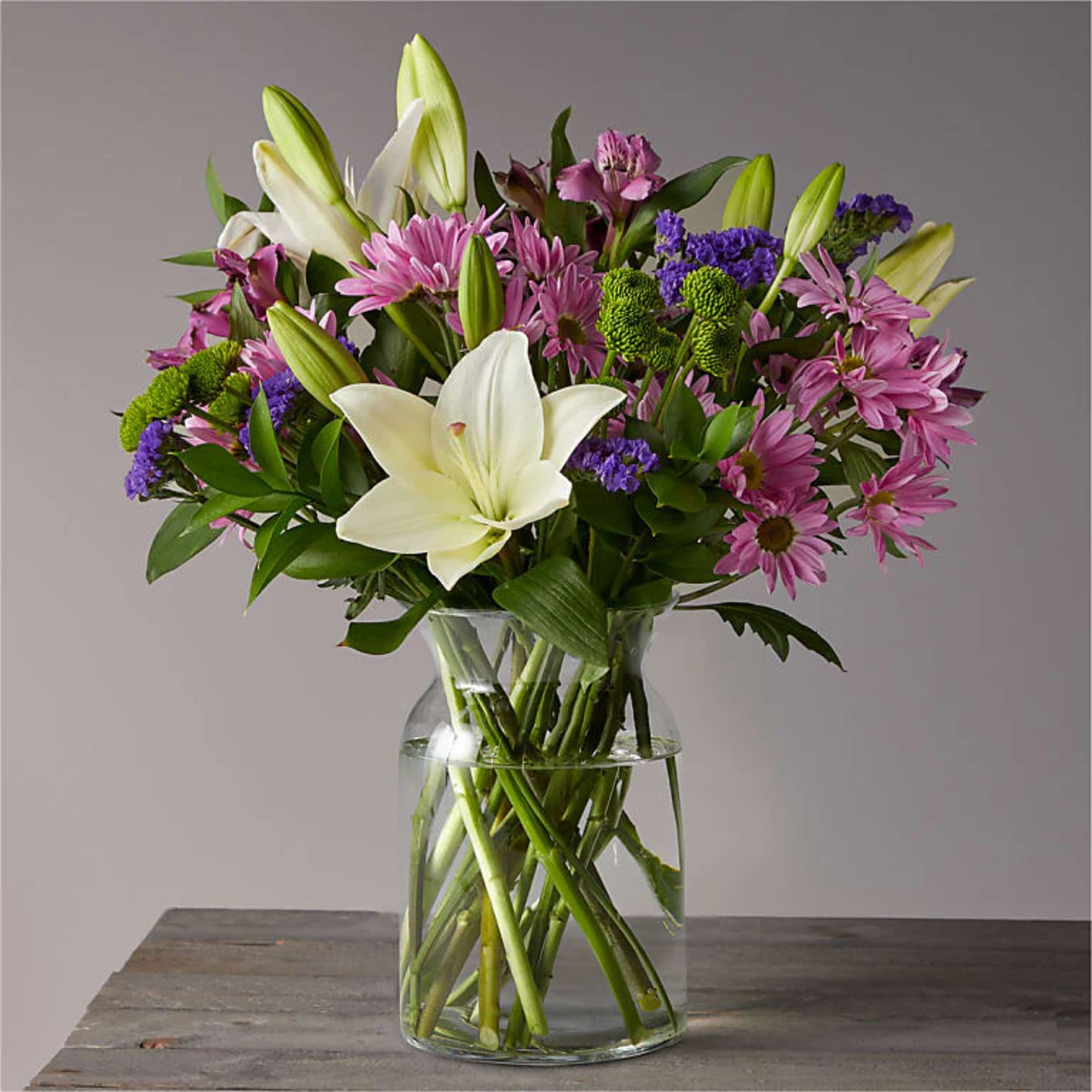 Bouquet of white lilies, pink daisies, and purple filler in a glass vase