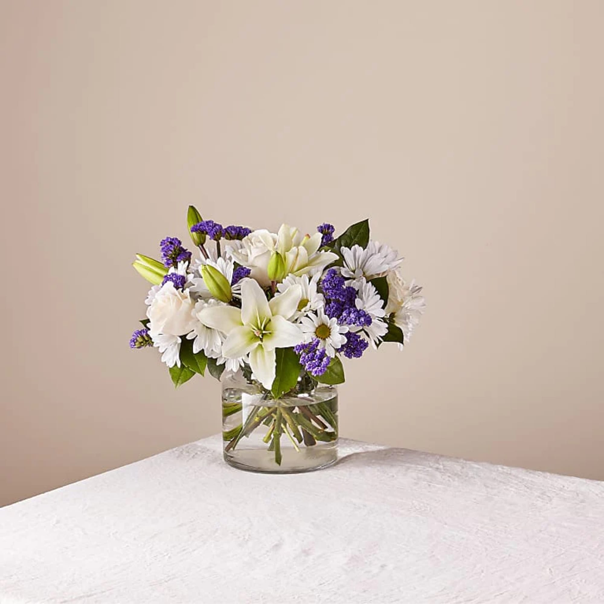 White lilies and daisies with purple filler in a glass vase