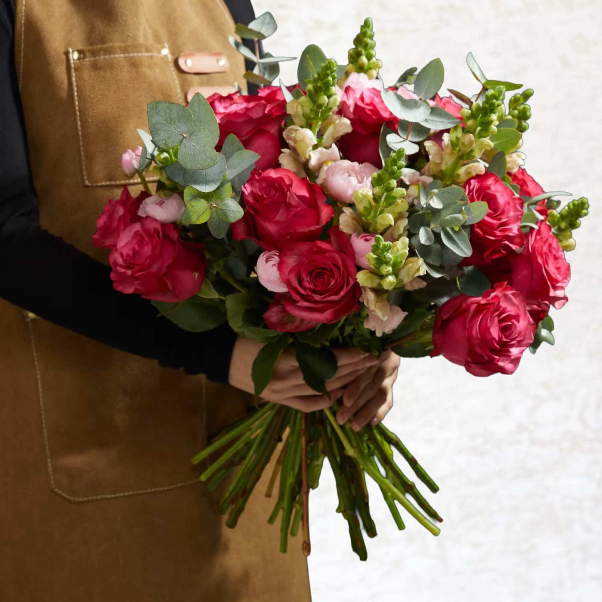 Handheld bouquet of red roses with pink blooms and eucalyptus