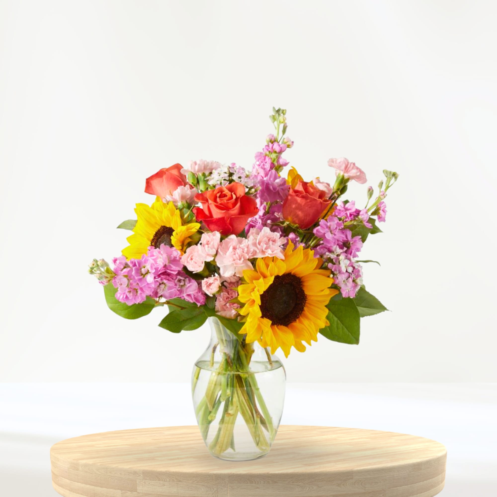 Bouquet of sunflowers, red roses, and pink flowers in a clear glass vase