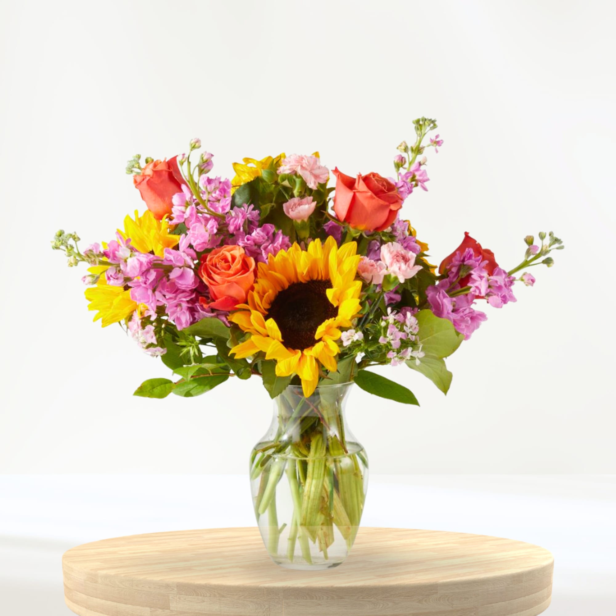 Mixed bouquet with sunflowers, roses, and pink flowers in a glass vase