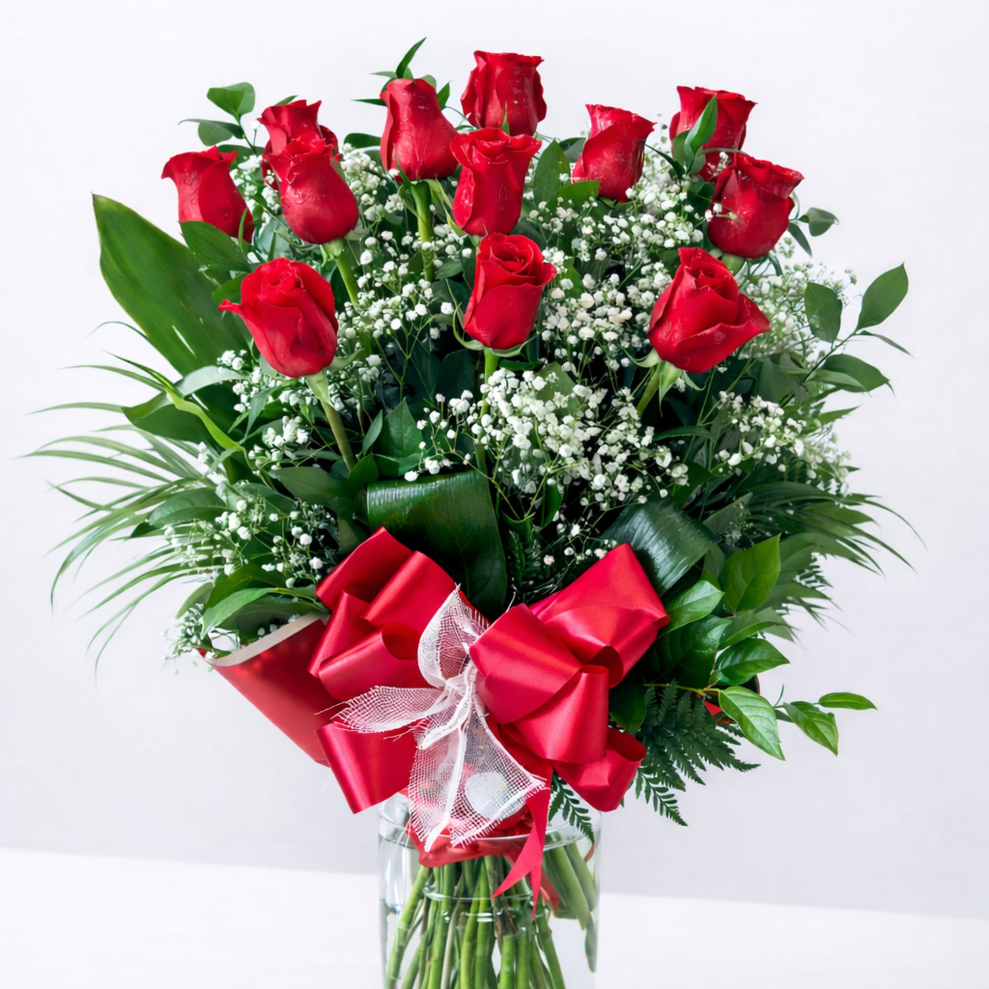 Red roses arranged in a clear glass vase with a red ribbon bow