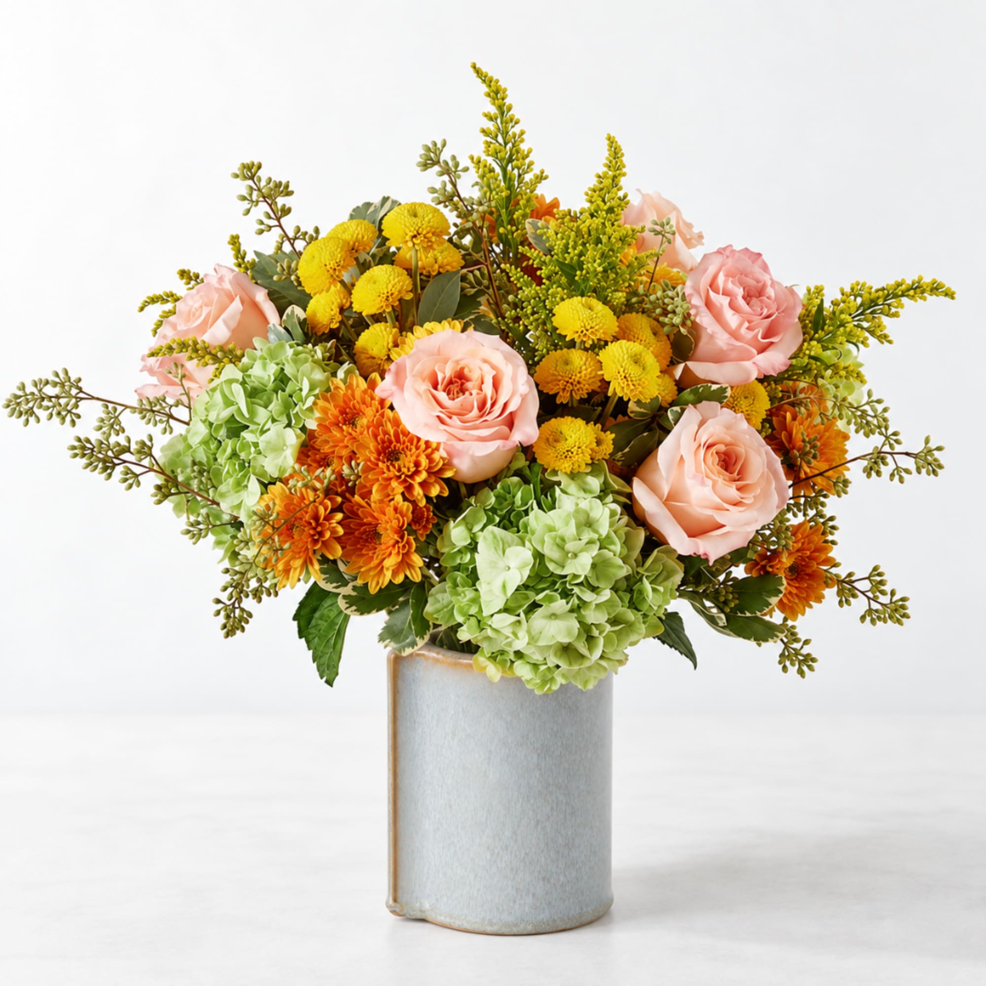 Mixed bouquet of pink roses, green hydrangeas, and yellow-orange blooms in a ceramic vase