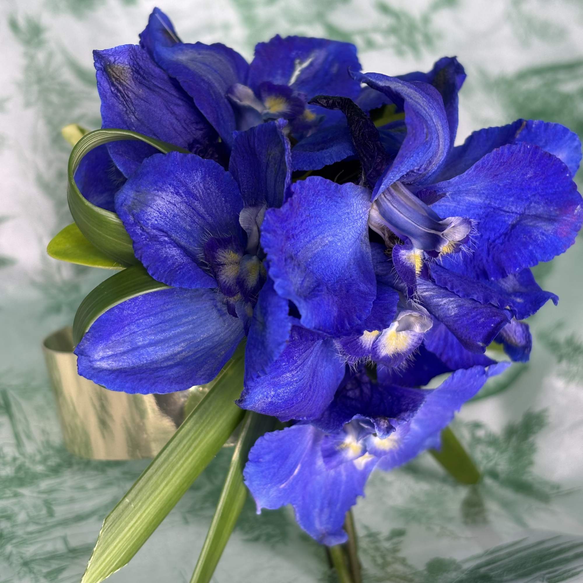 Blue orchid bouquet with green leaves in a gold wrap