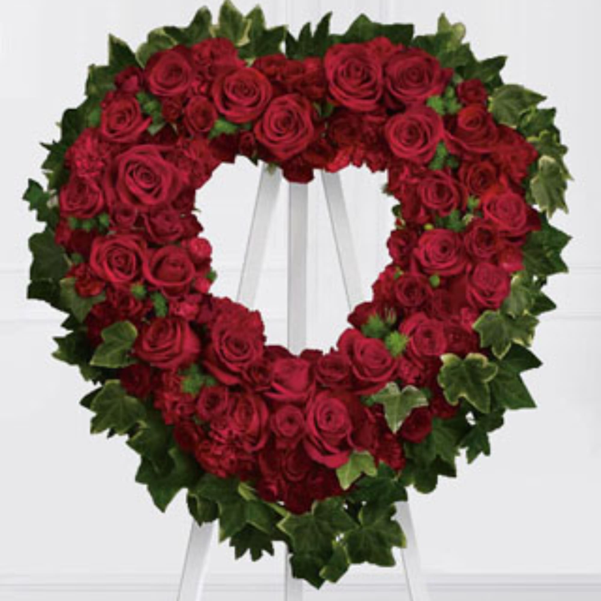 Heart-shaped wreath of red roses with green ivy on a white stand