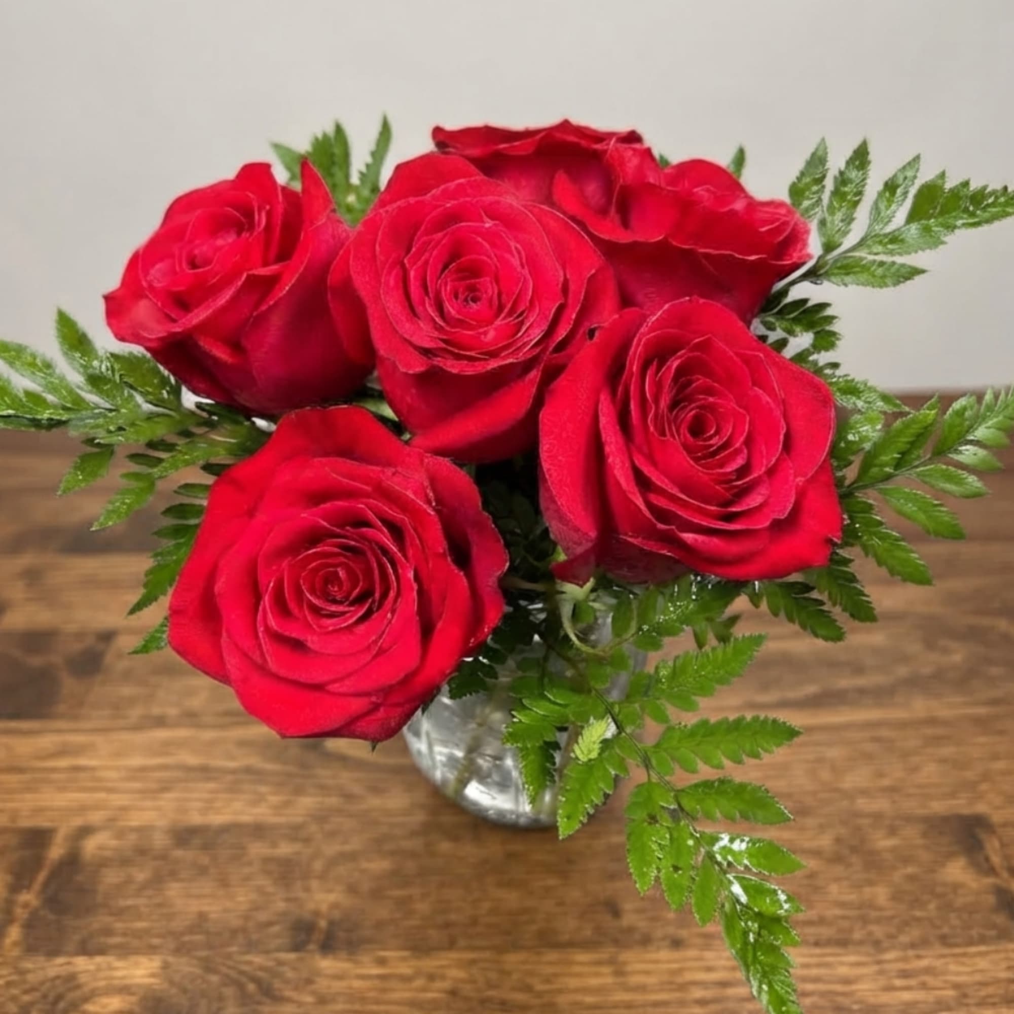 Red roses arranged in a small glass vase with fern foliage