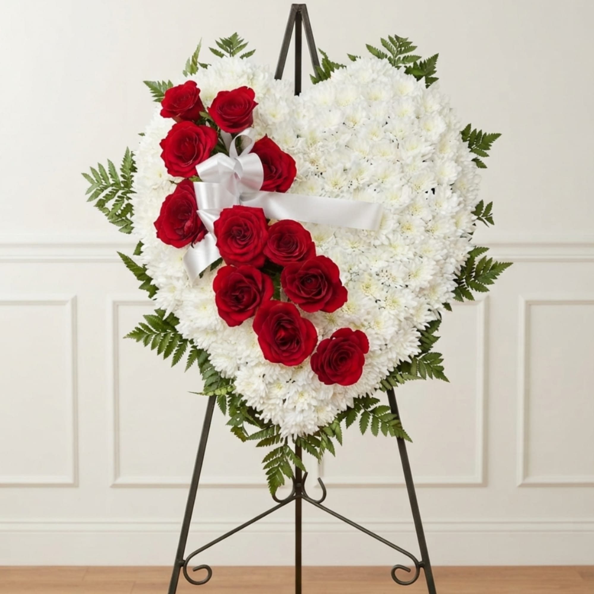 Heart-shaped white chrysanthemum wreath with red roses and a white ribbon on an easel