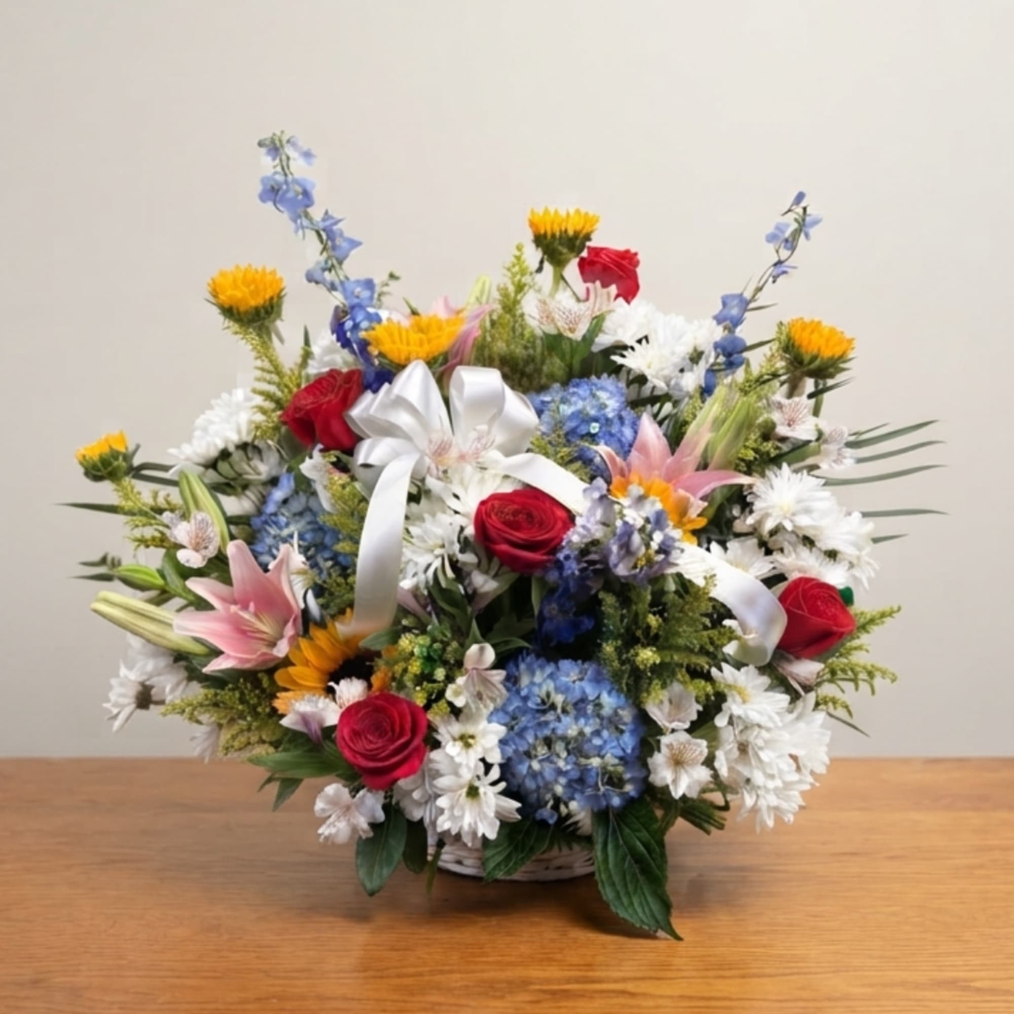 Mixed bouquet in a basket with red roses, blue hydrangeas, white daisies, and a white ribbon