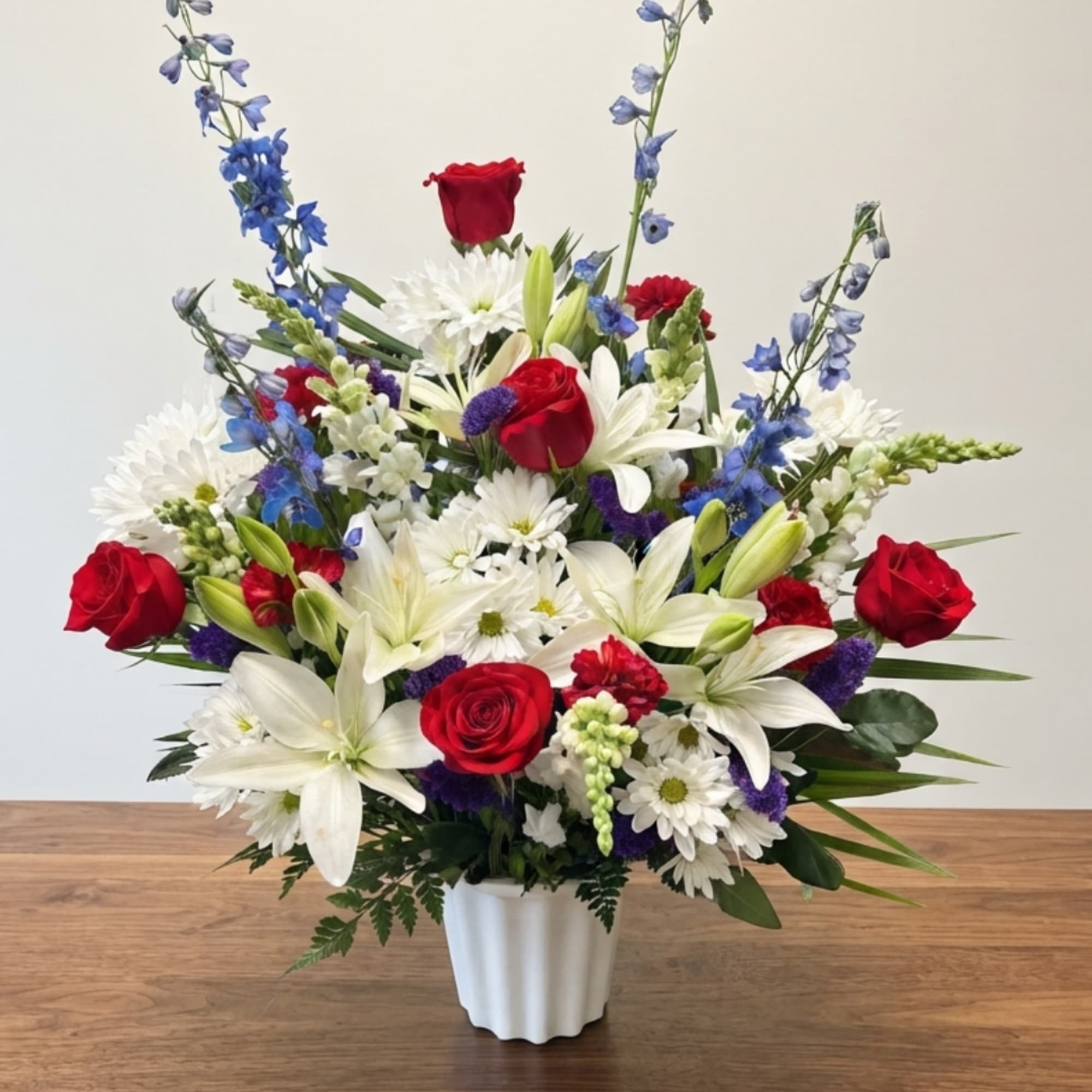 Red roses and white lilies in a white vase with blue flowers