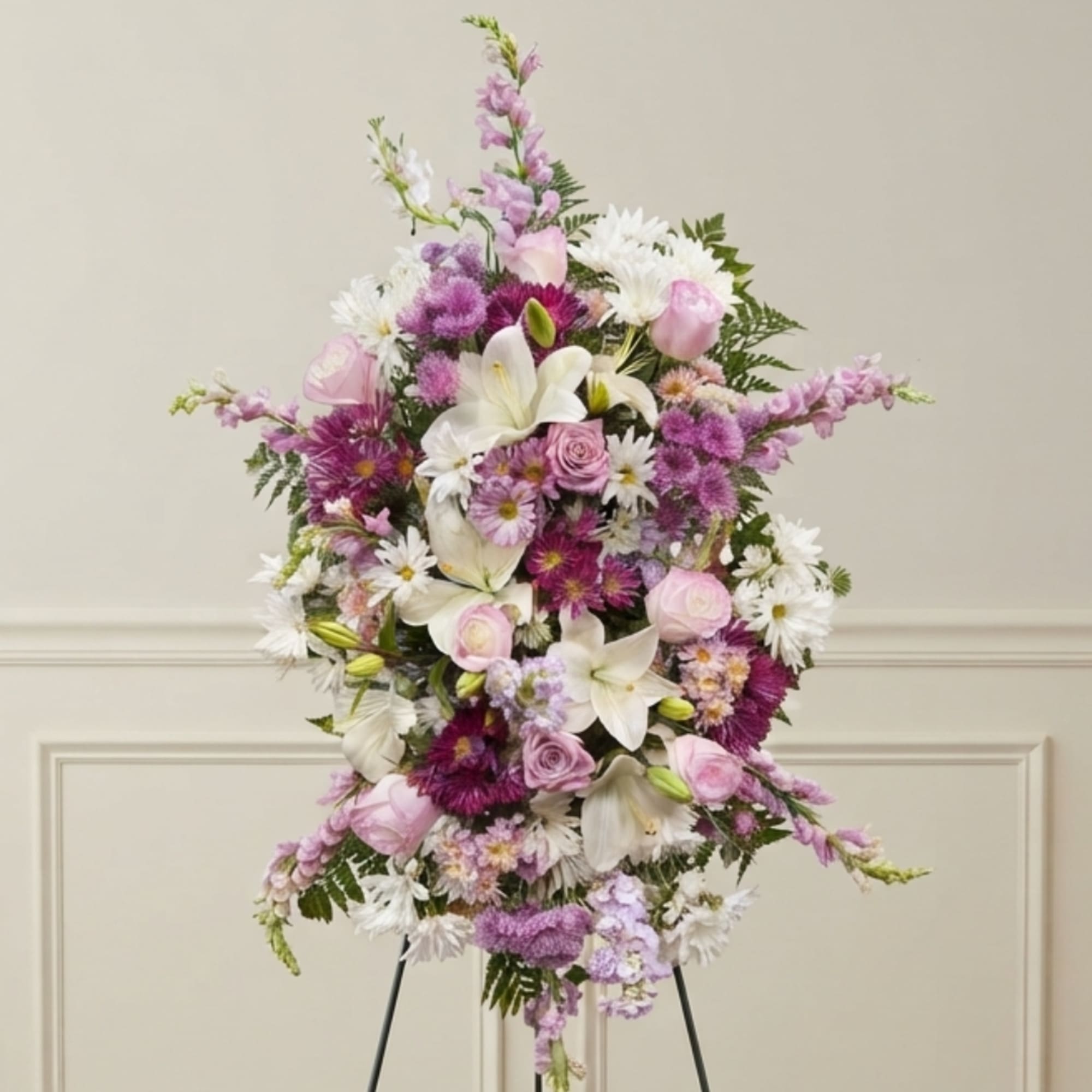 Tall pastel floral spray with white lilies, pink roses, and purple blooms on an easel