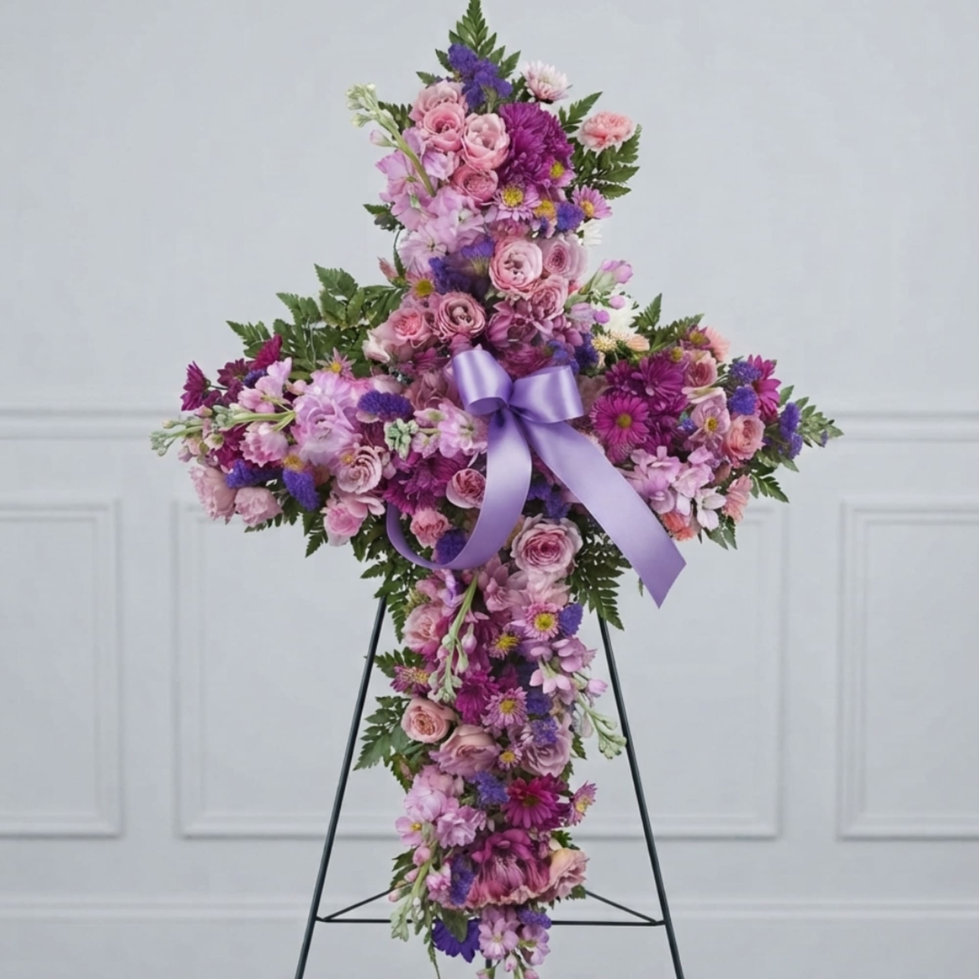 Cross-shaped floral tribute with pink and purple flowers and a lavender ribbon