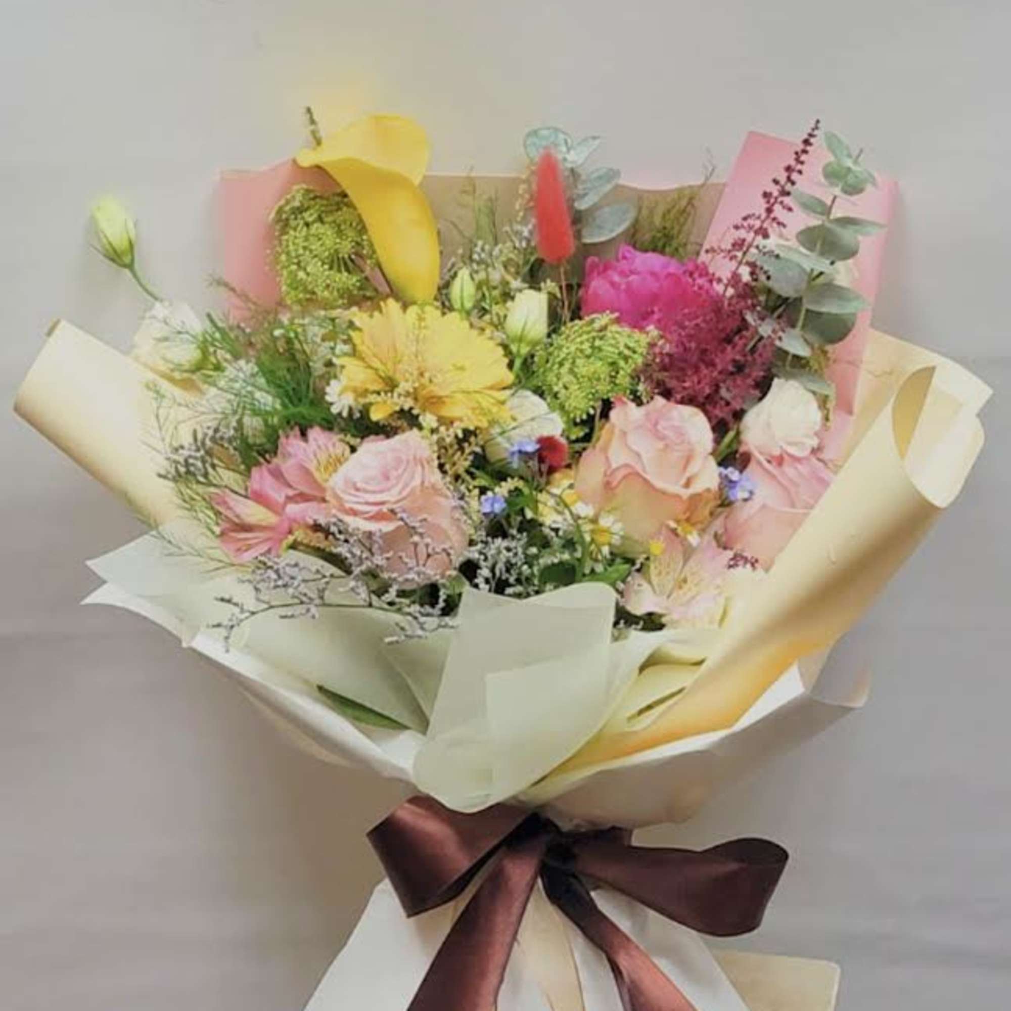 Mixed bouquet with pink roses, yellow calla lilies, and greenery wrapped in paper