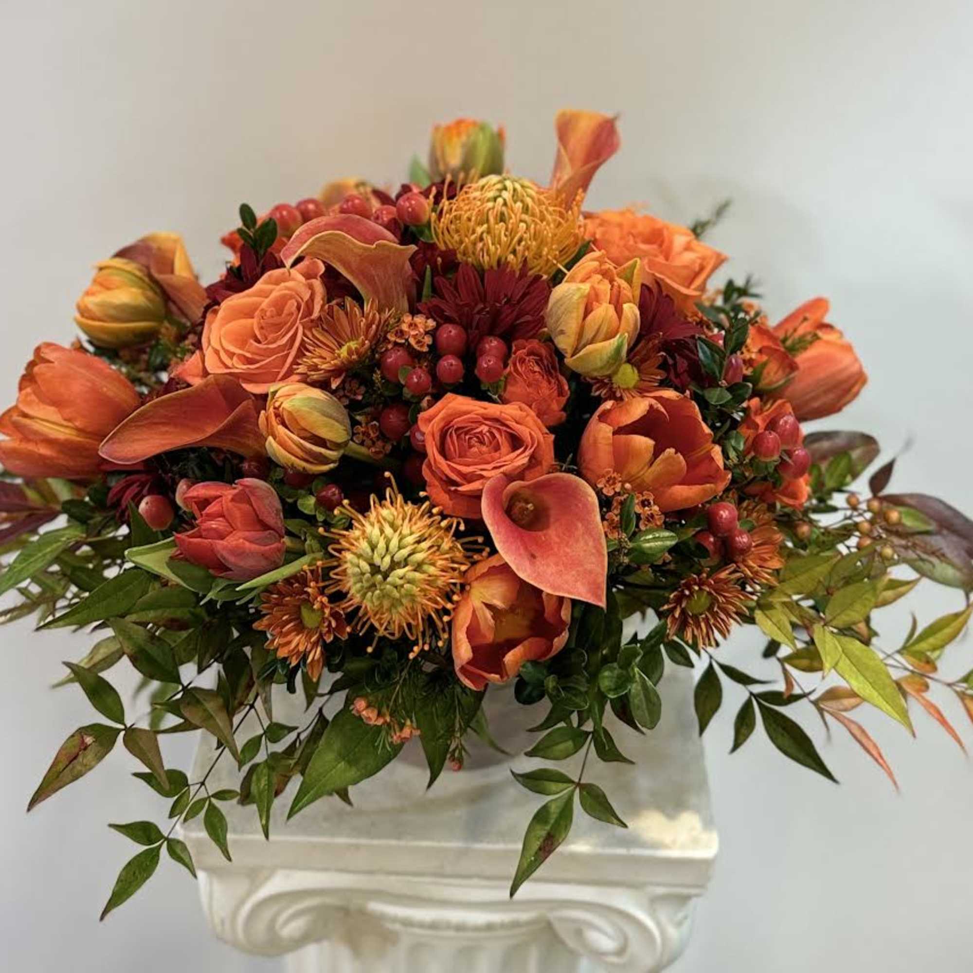 Orange floral arrangement with roses, calla lilies, and berries in a white vase
