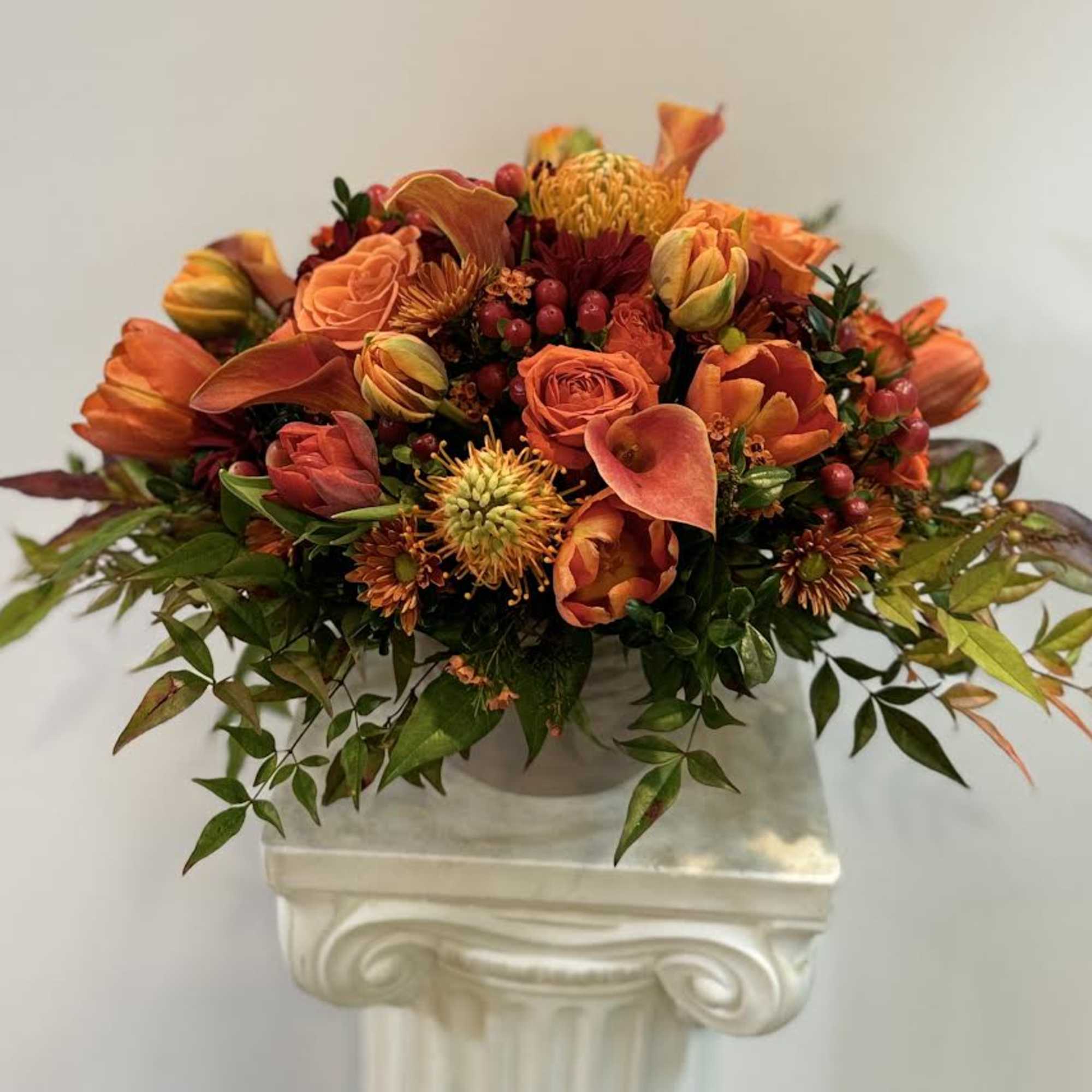 Orange floral arrangement in a white pedestal vase