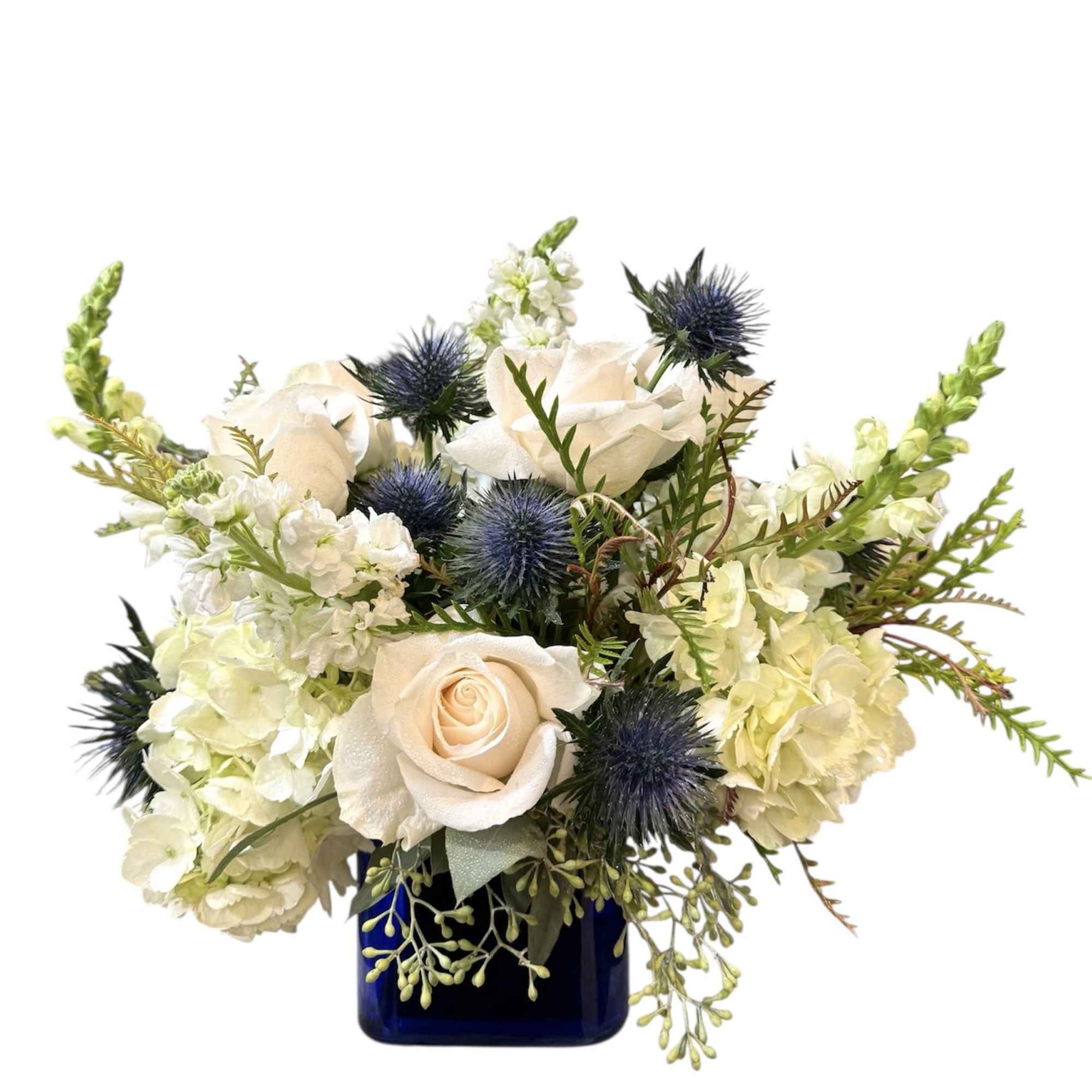 White roses and pale blooms in a blue vase with spiky blue thistles