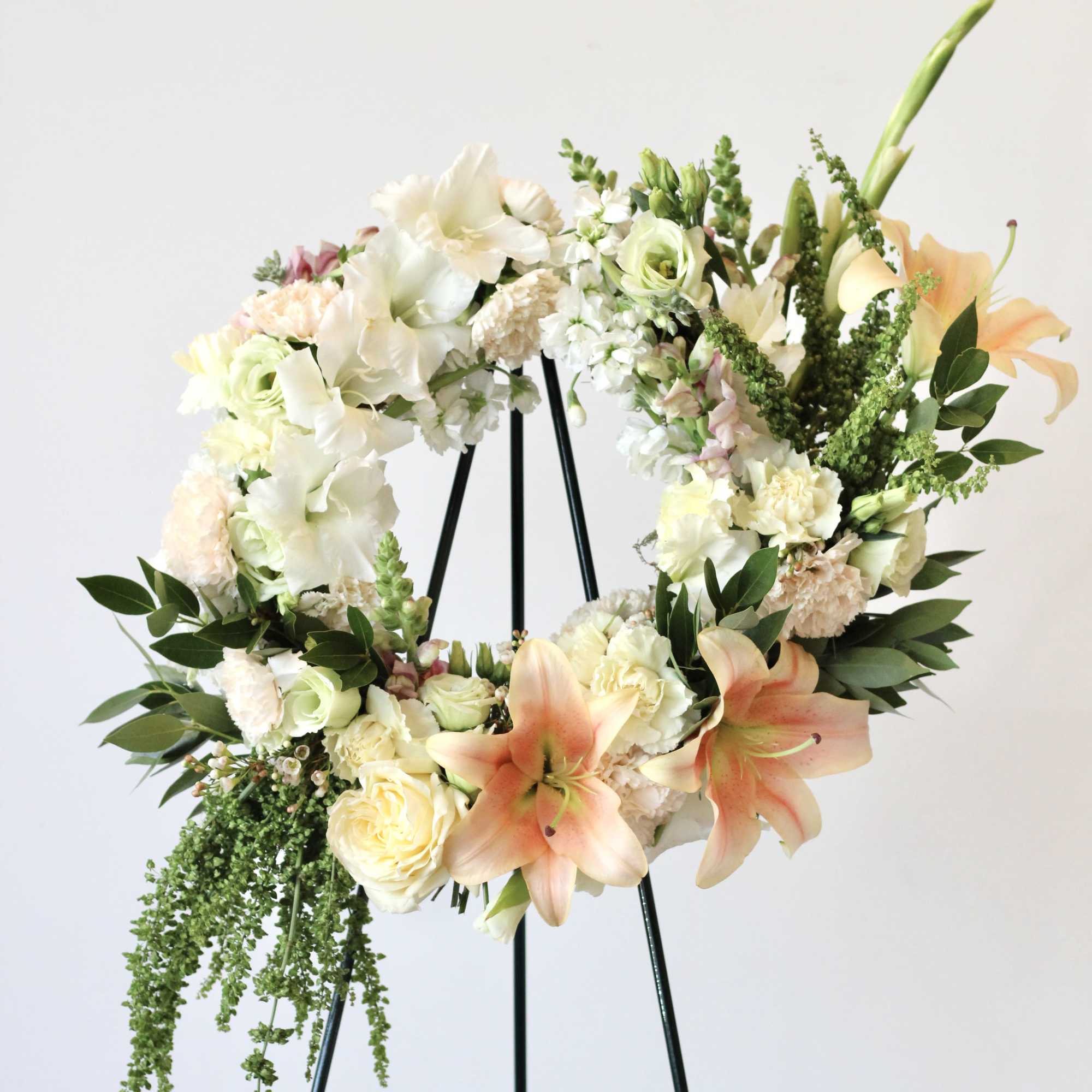 Floral wreath with white and peach blooms on a black stand
