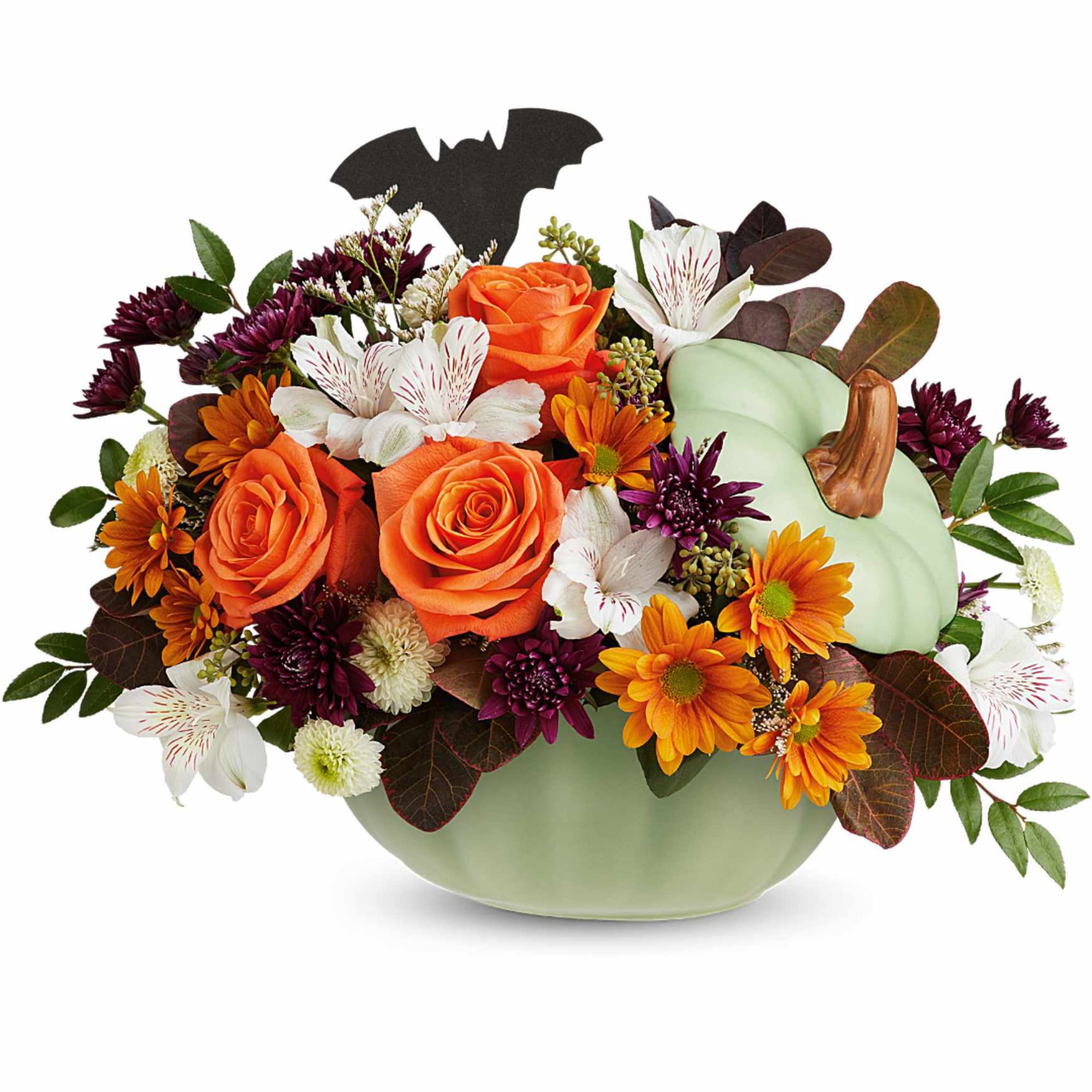 Orange roses and mixed flowers arranged in a pale green pumpkin vase with a bat topper