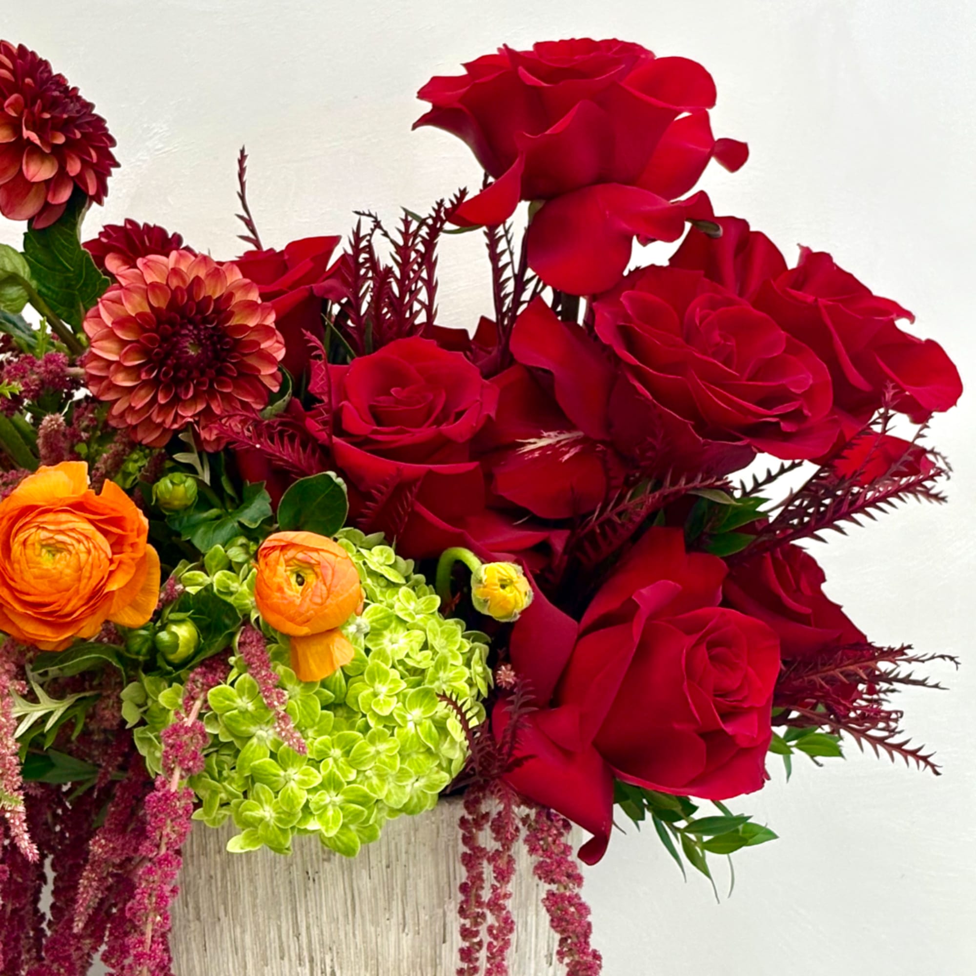Bouquet of red roses, orange ranunculus, and green hydrangea in a vase