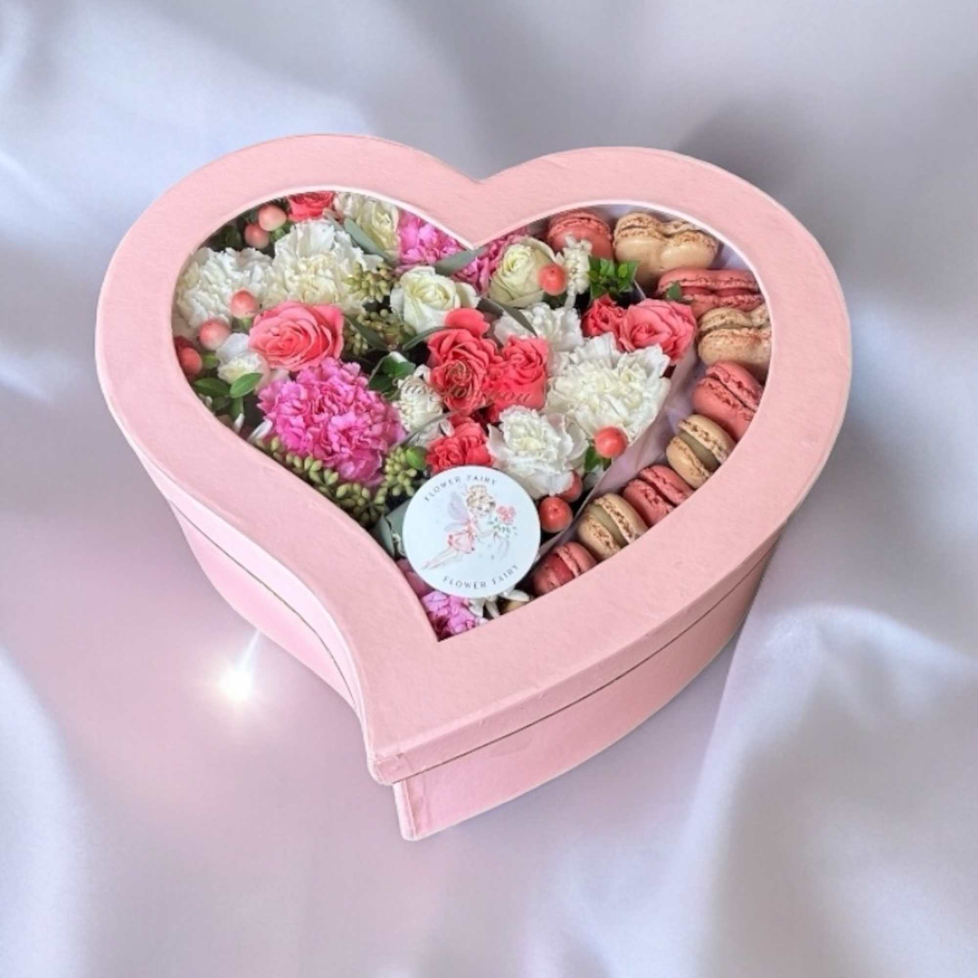 Heart-shaped pink box filled with pink and white flowers and macarons