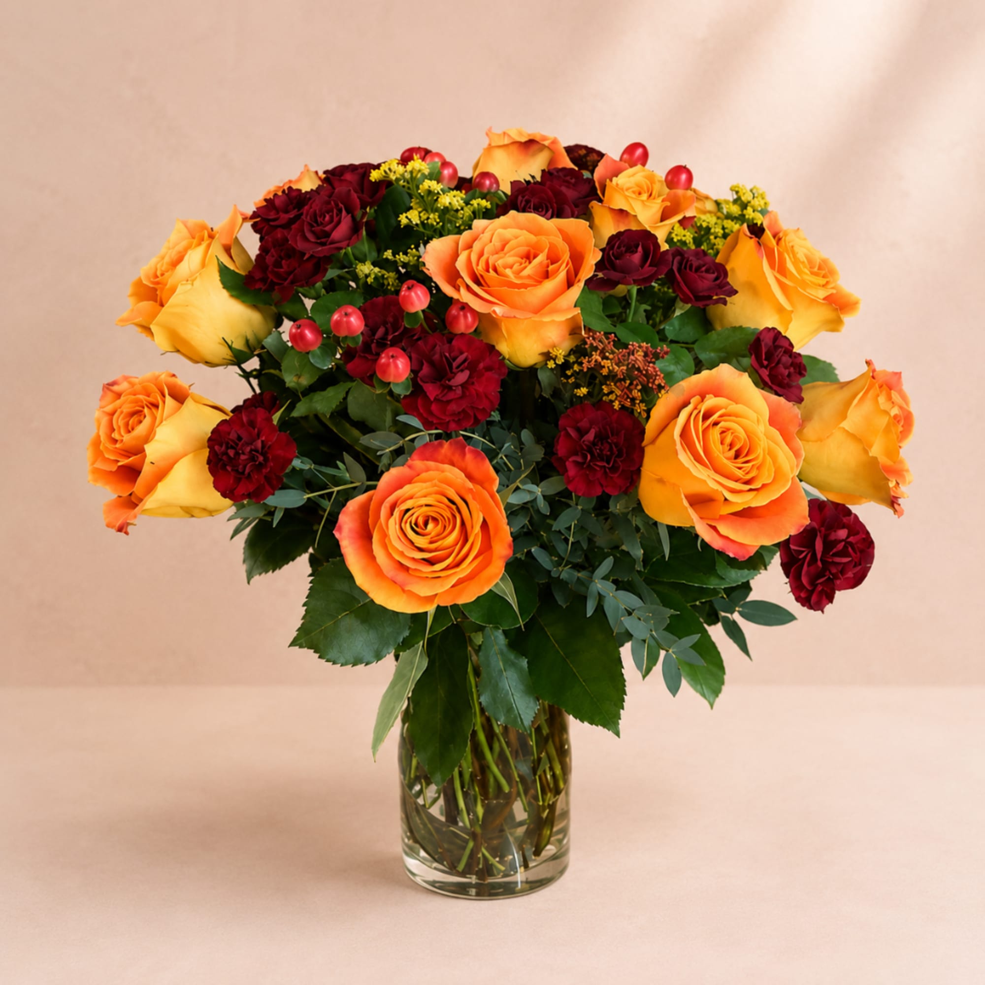 Orange and burgundy roses in a clear glass vase