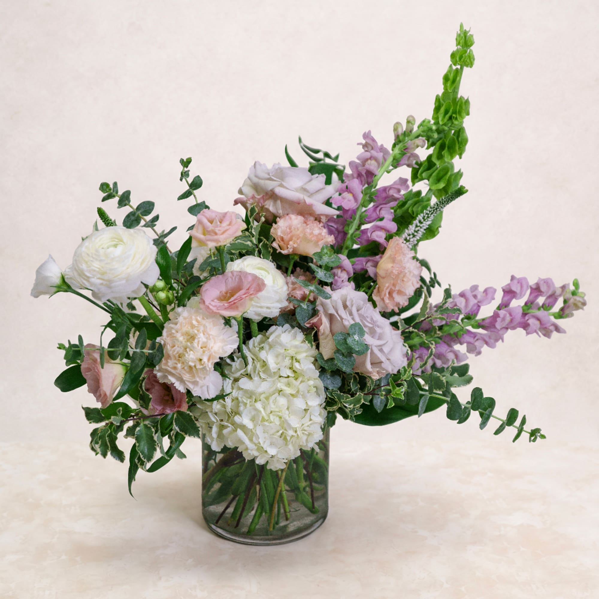 Pastel bouquet of roses, hydrangea, and snapdragons in a clear glass vase