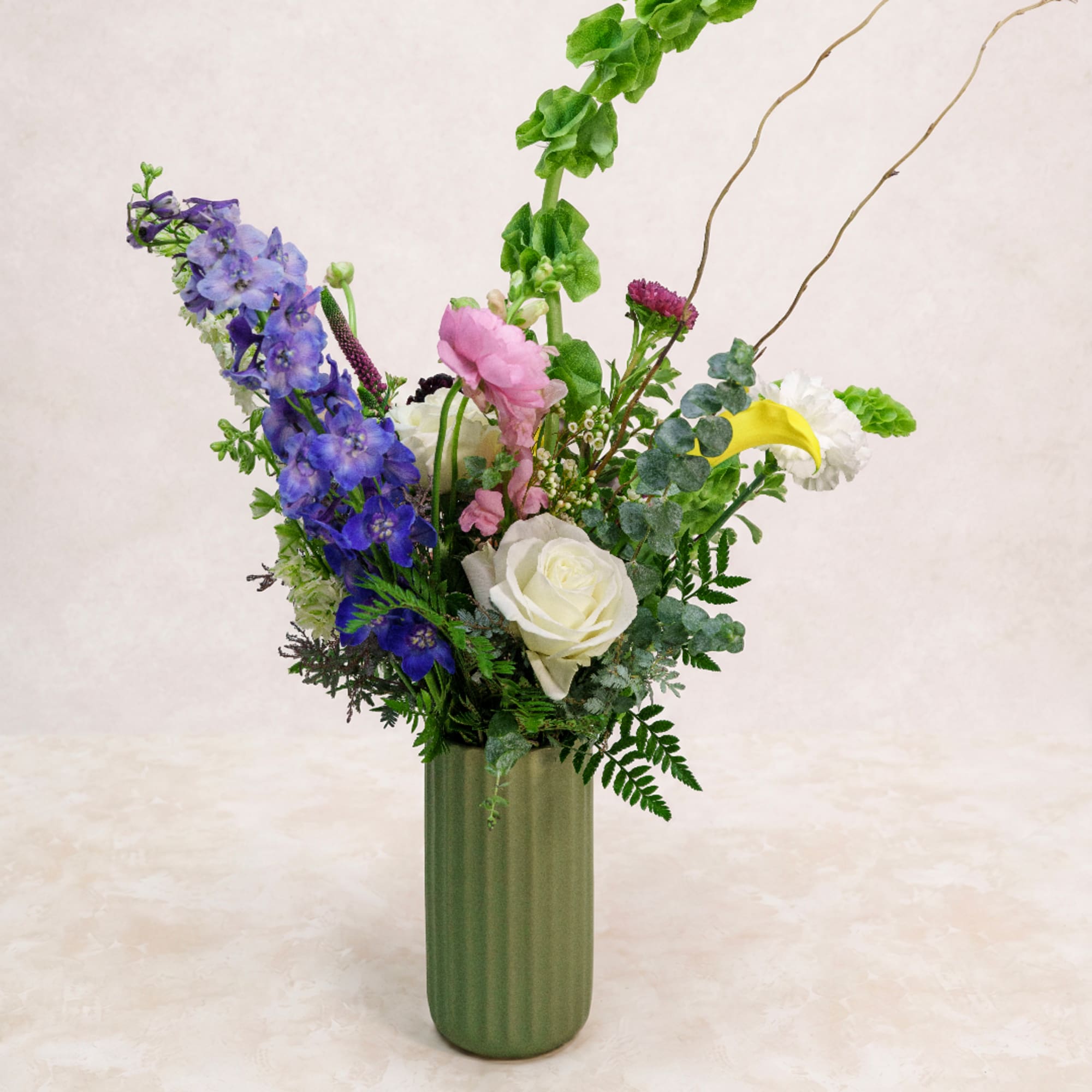 Mixed bouquet in a tall green vase with blue, pink, white, and yellow flowers