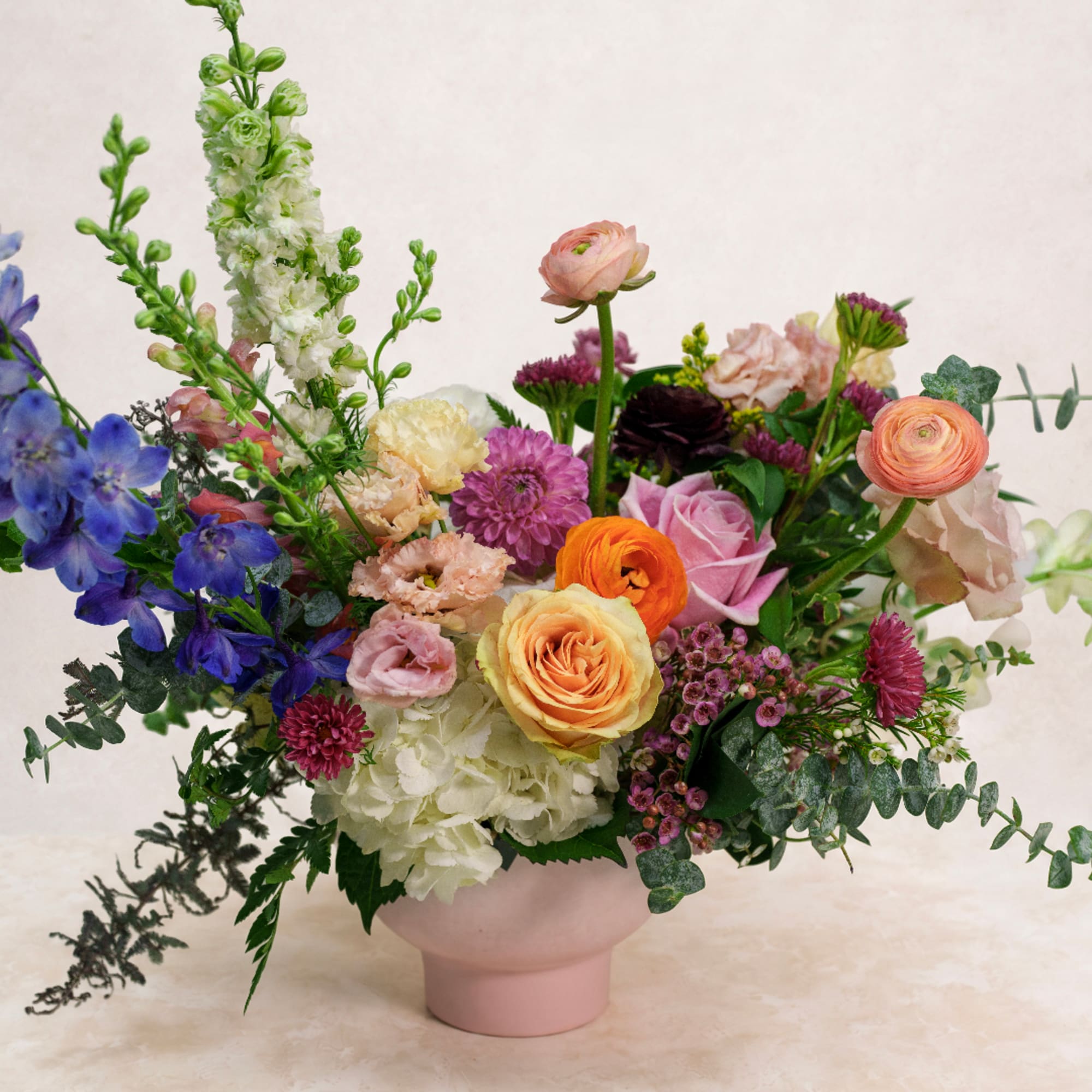 Mixed bouquet in a pink vase with blue, pink, orange, and white flowers