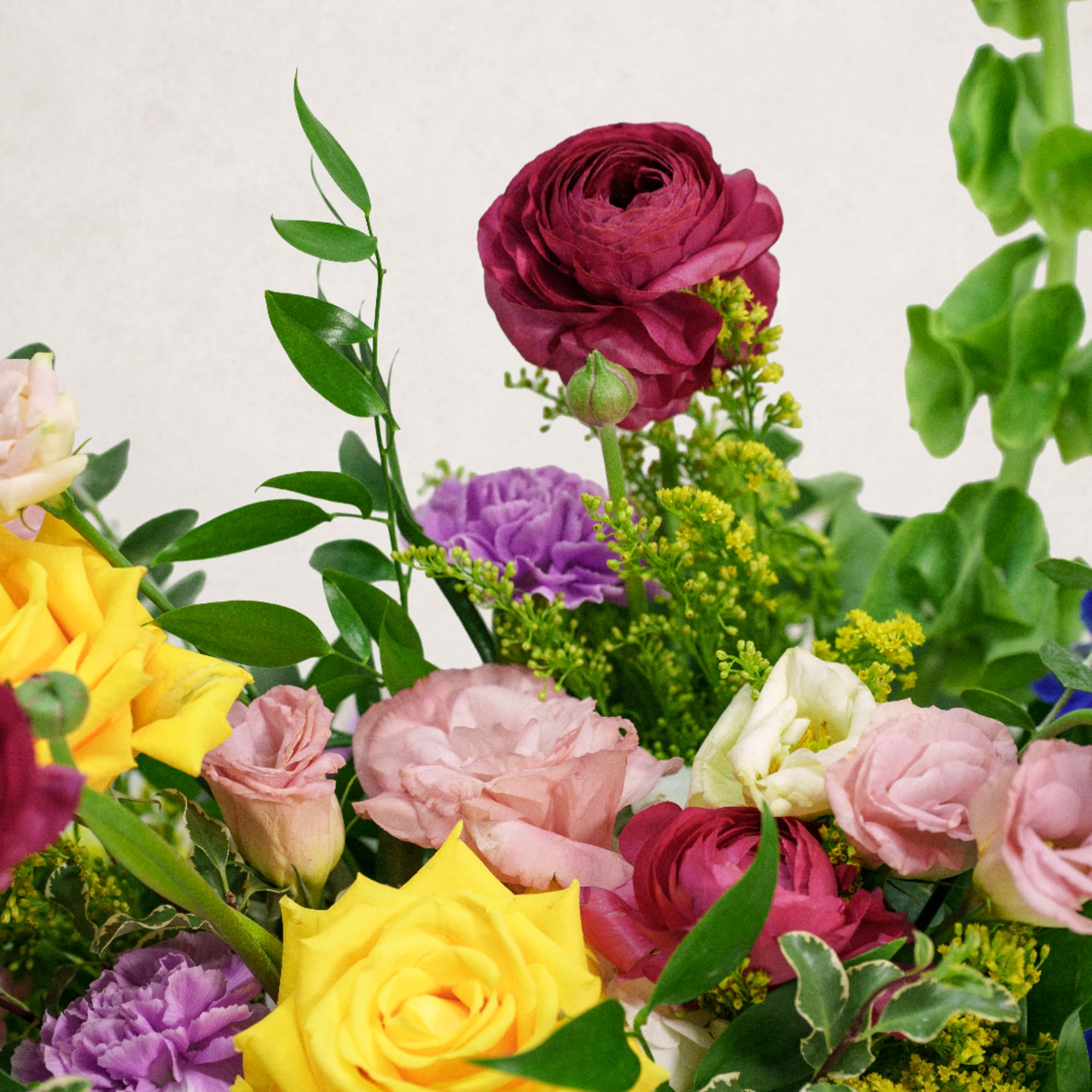 Mixed bouquet with roses, ranunculus, and carnations in pink, yellow, purple, and white.