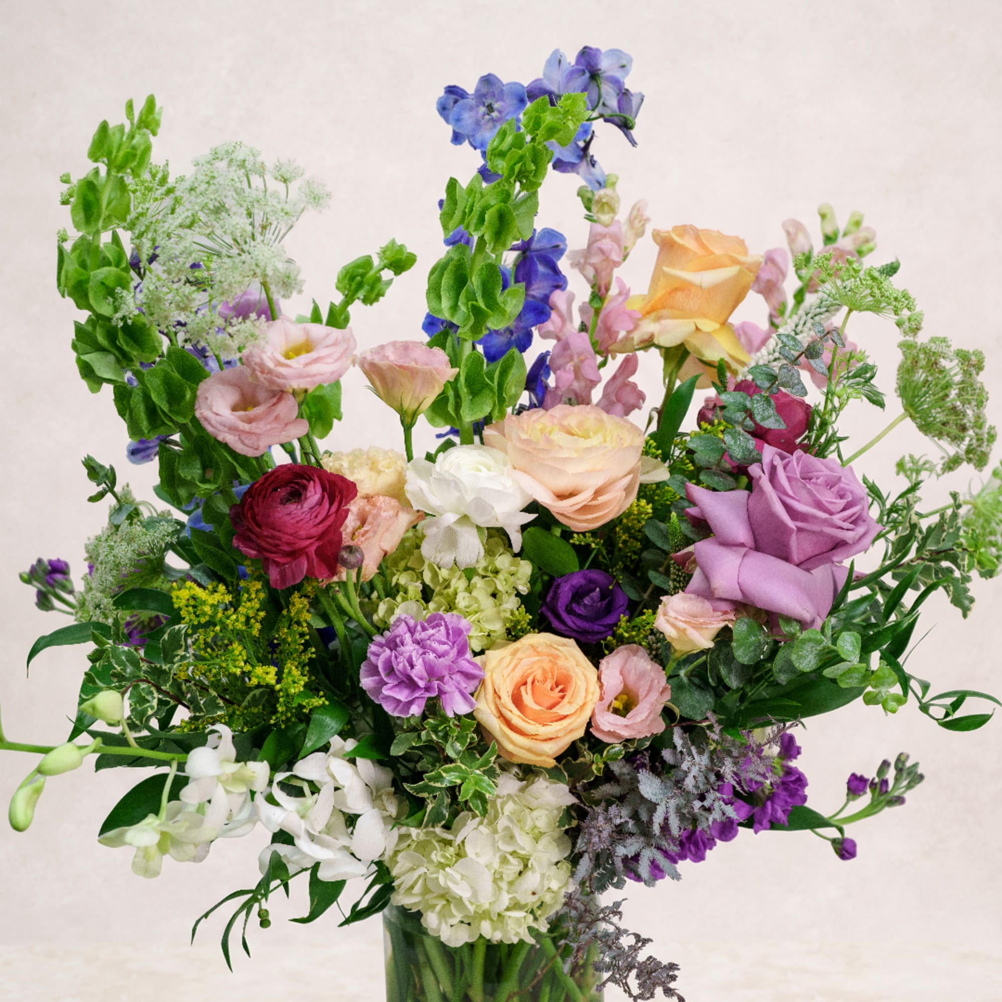 Mixed bouquet of roses, lisianthus, and delphinium in a glass vase
