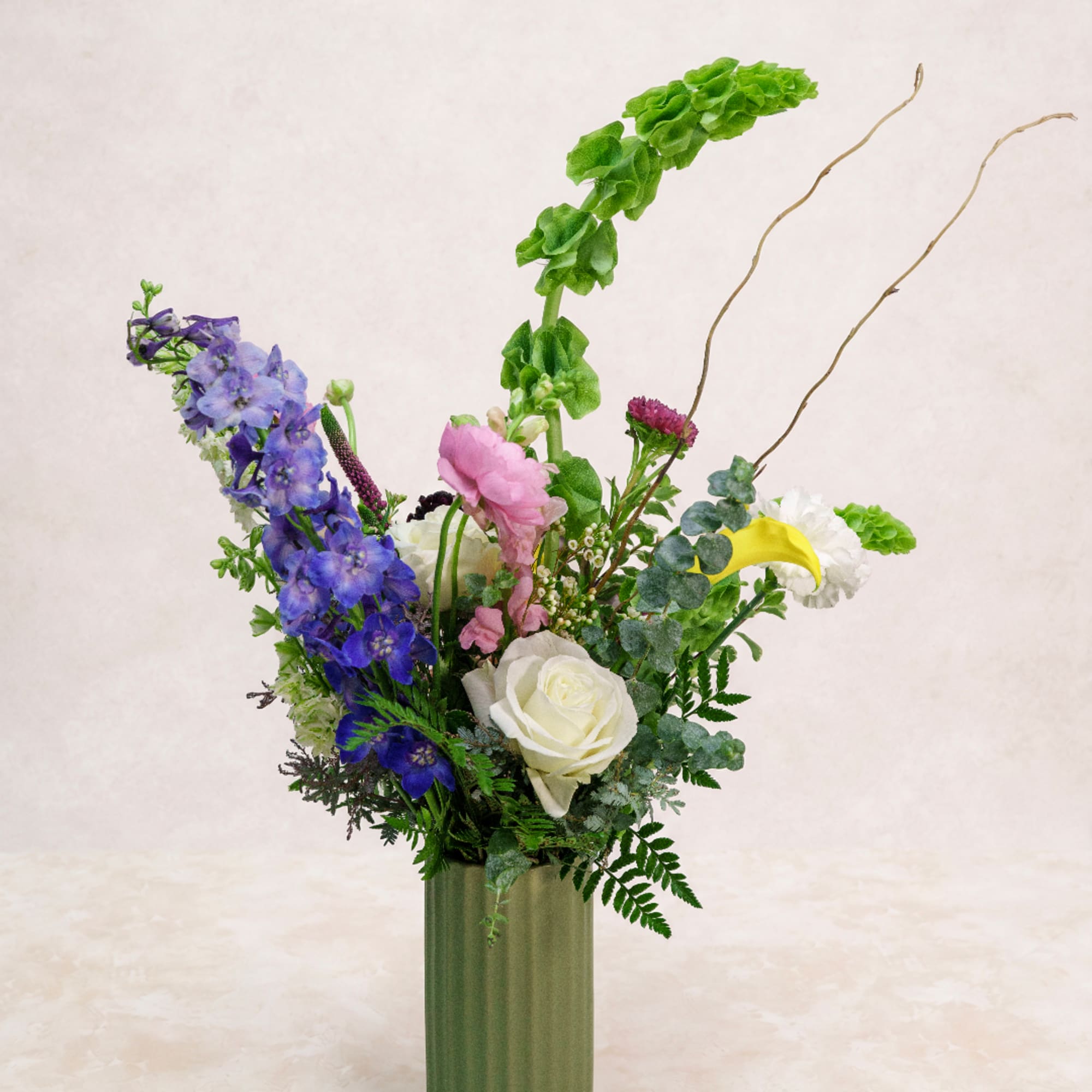 Tall mixed floral arrangement in a green vase with blue, pink, white, and yellow blooms