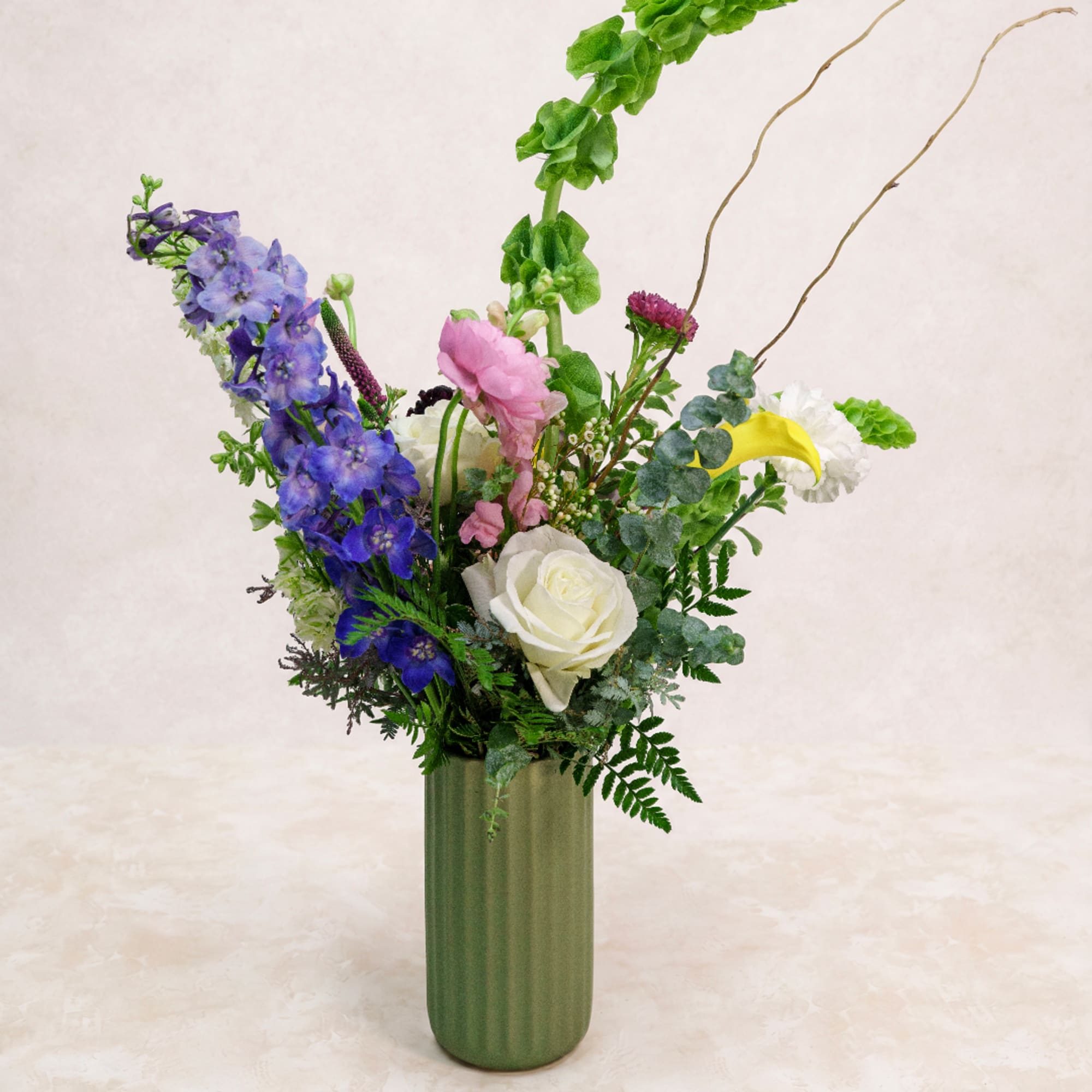 Tall mixed bouquet in a green vase with blue, pink, and white flowers