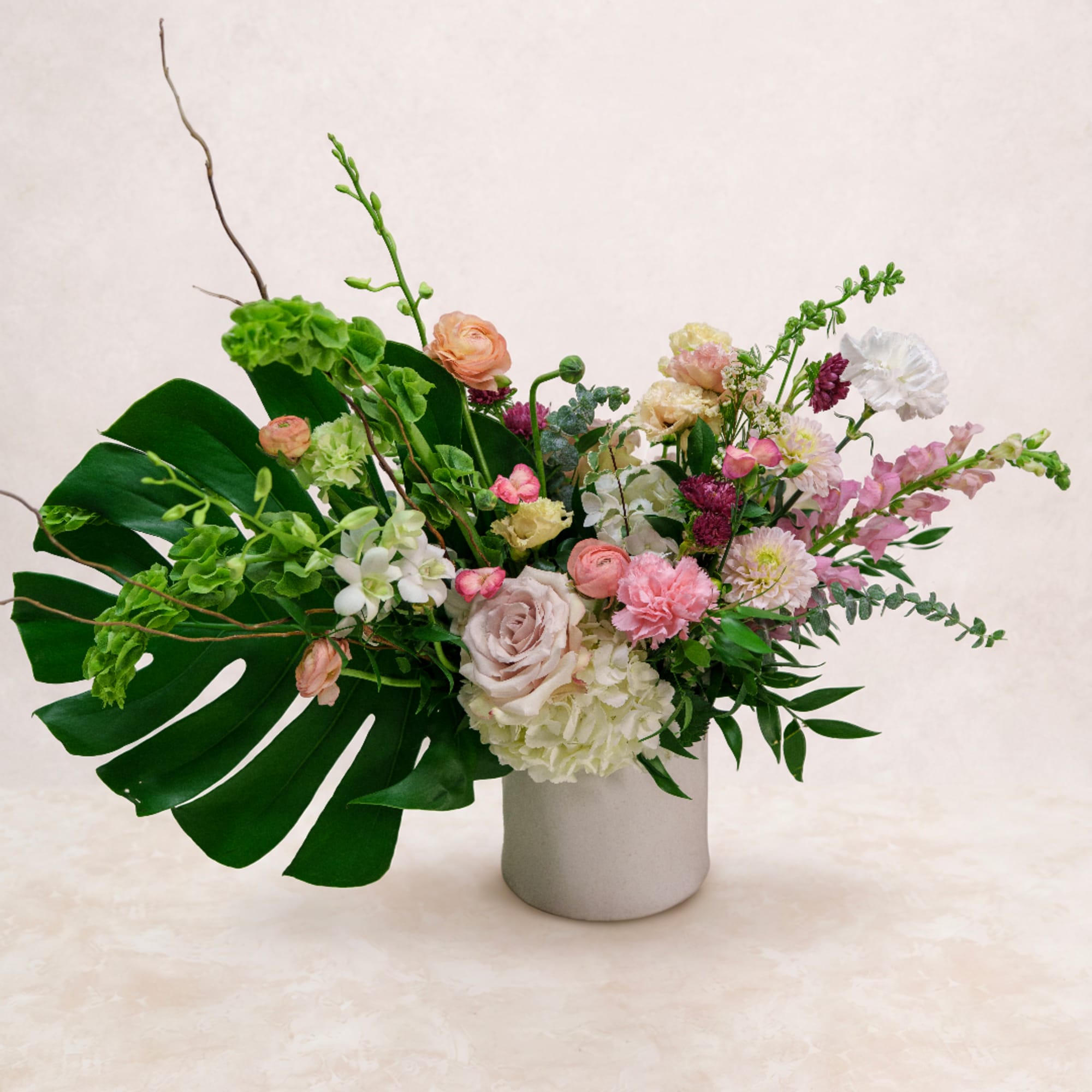 Mixed pastel flower arrangement in a gray vase with large tropical leaves
