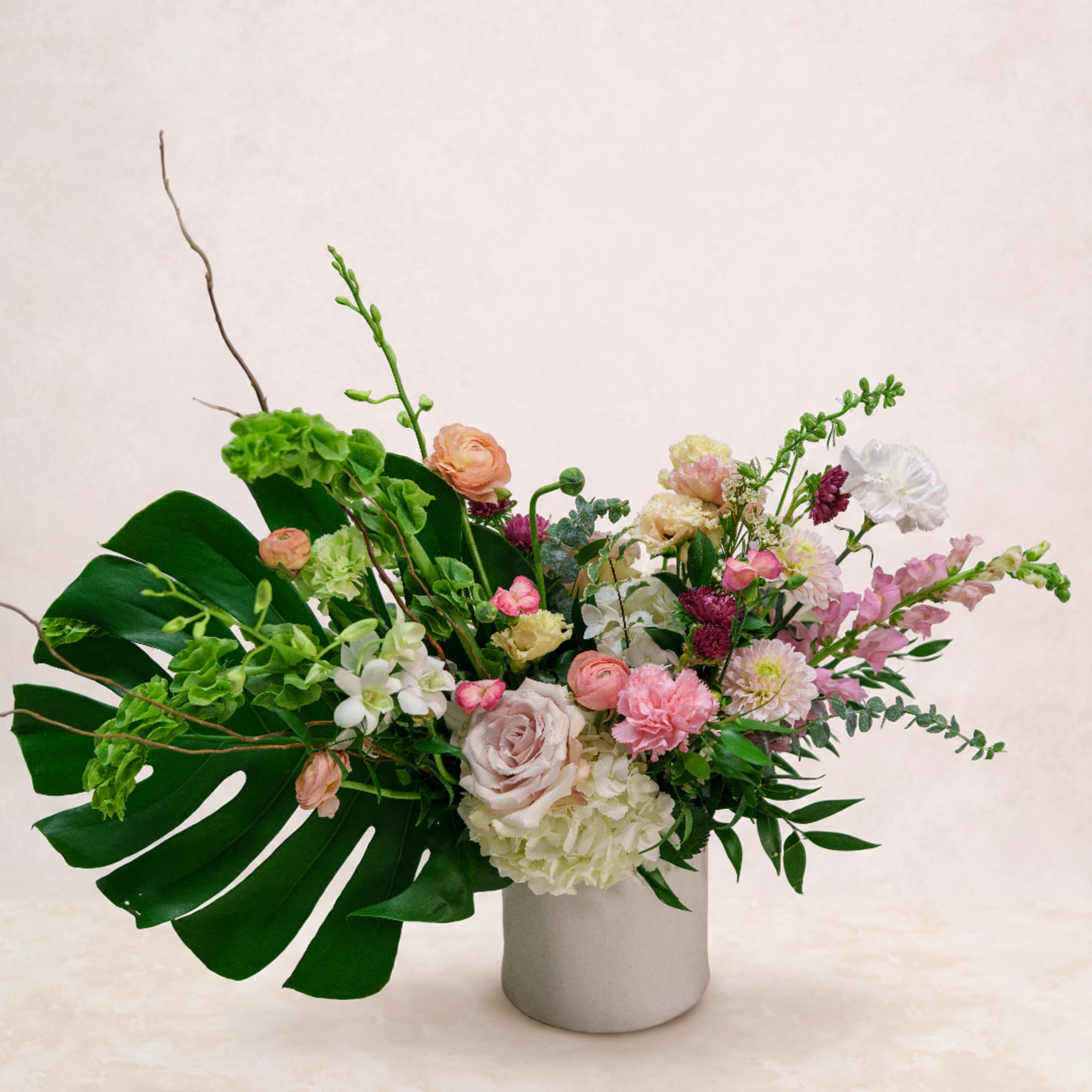 Mixed pastel flower arrangement in a white vase with large tropical leaves