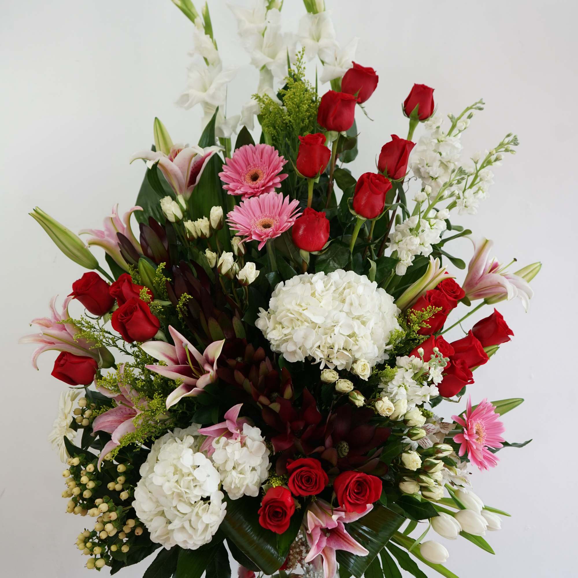Tall arrangement of red roses, white hydrangeas, pink lilies and gerbera daisies in a clear glass vase