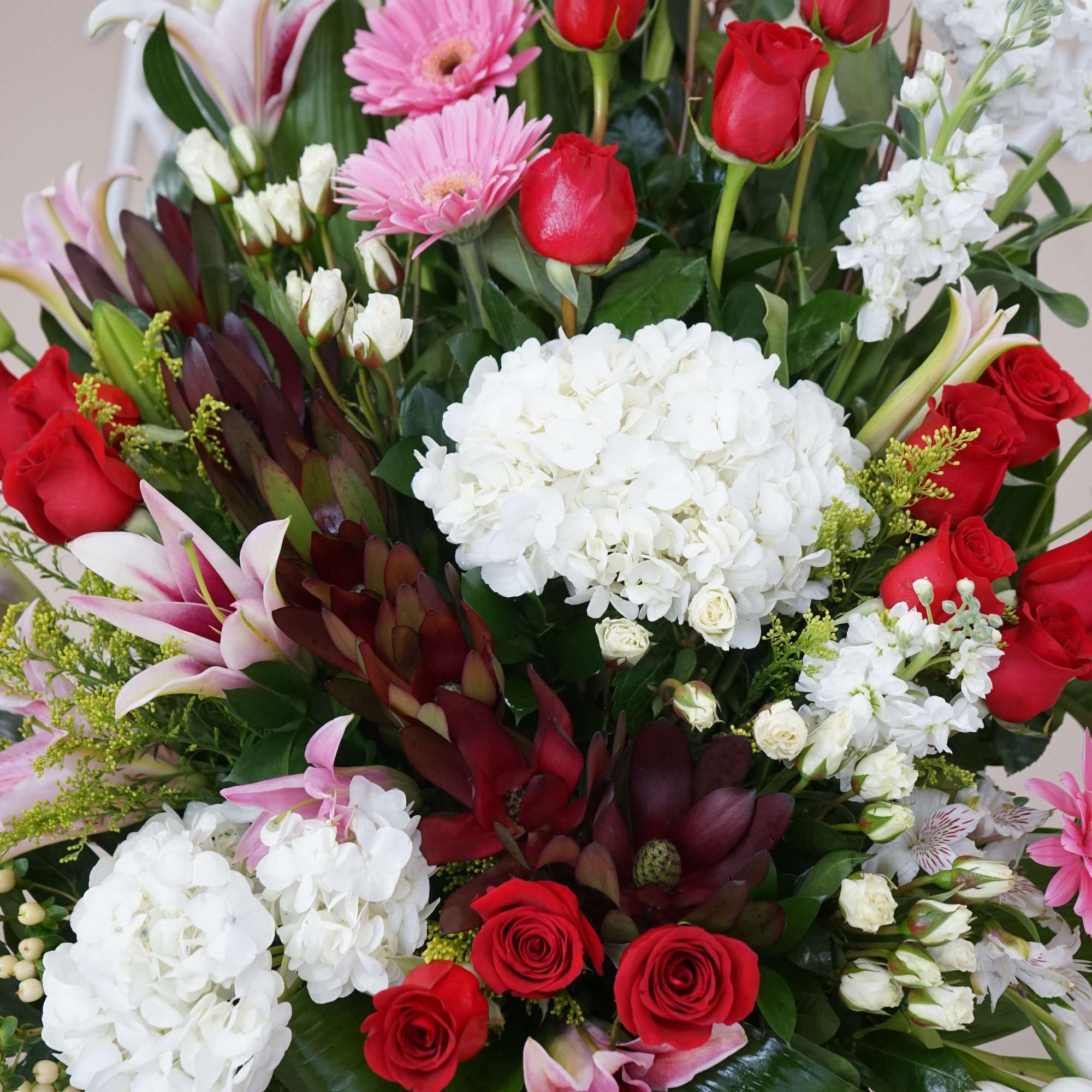 Tall mixed arrangement of red roses, white hydrangeas, pink gerbera daisies and lilies in a clear glass vase