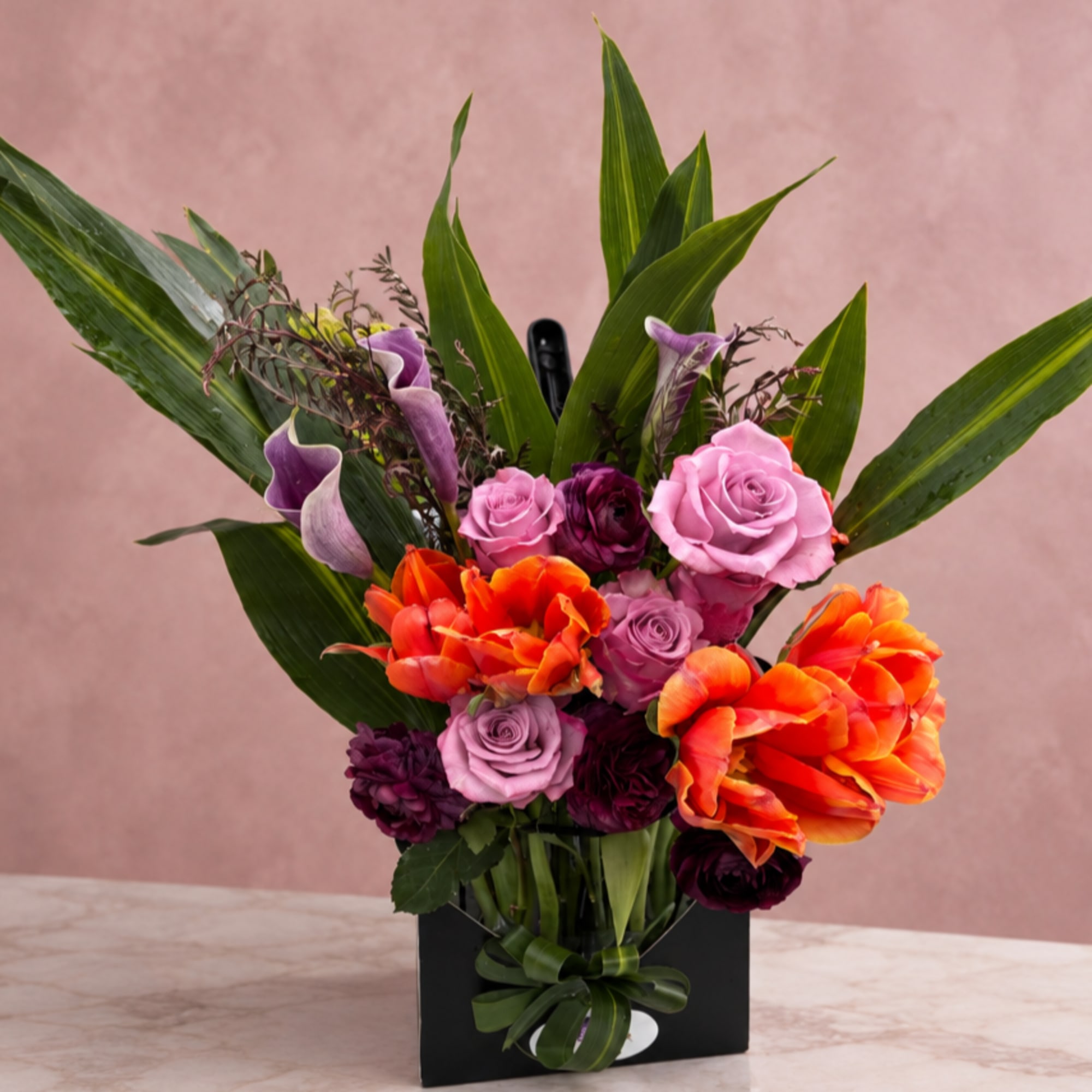 Bouquet of pink and orange flowers in a black box with a ribbon