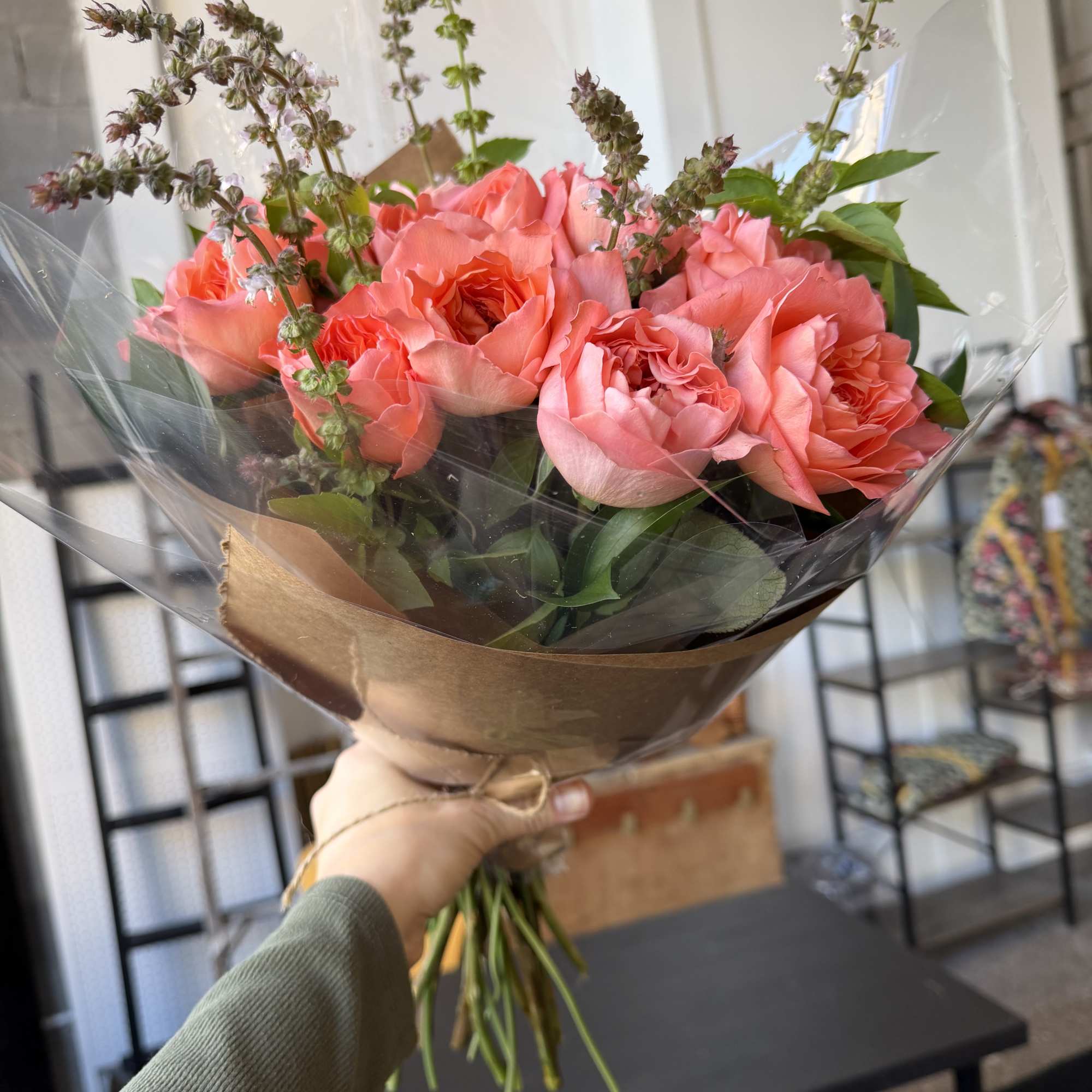 Handheld bouquet of pink roses wrapped in brown paper and clear plastic
