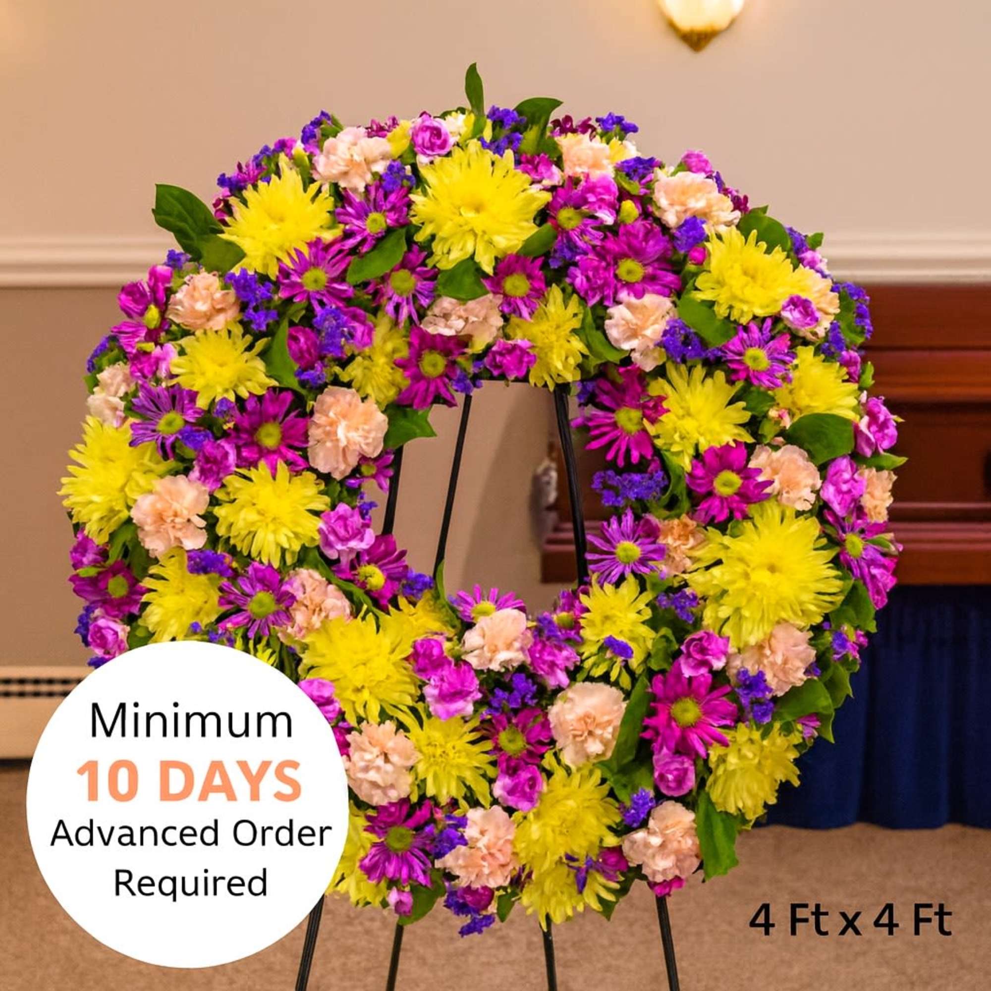 Large standing wreath of yellow, pink, peach, and purple flowers on a metal easel indoors