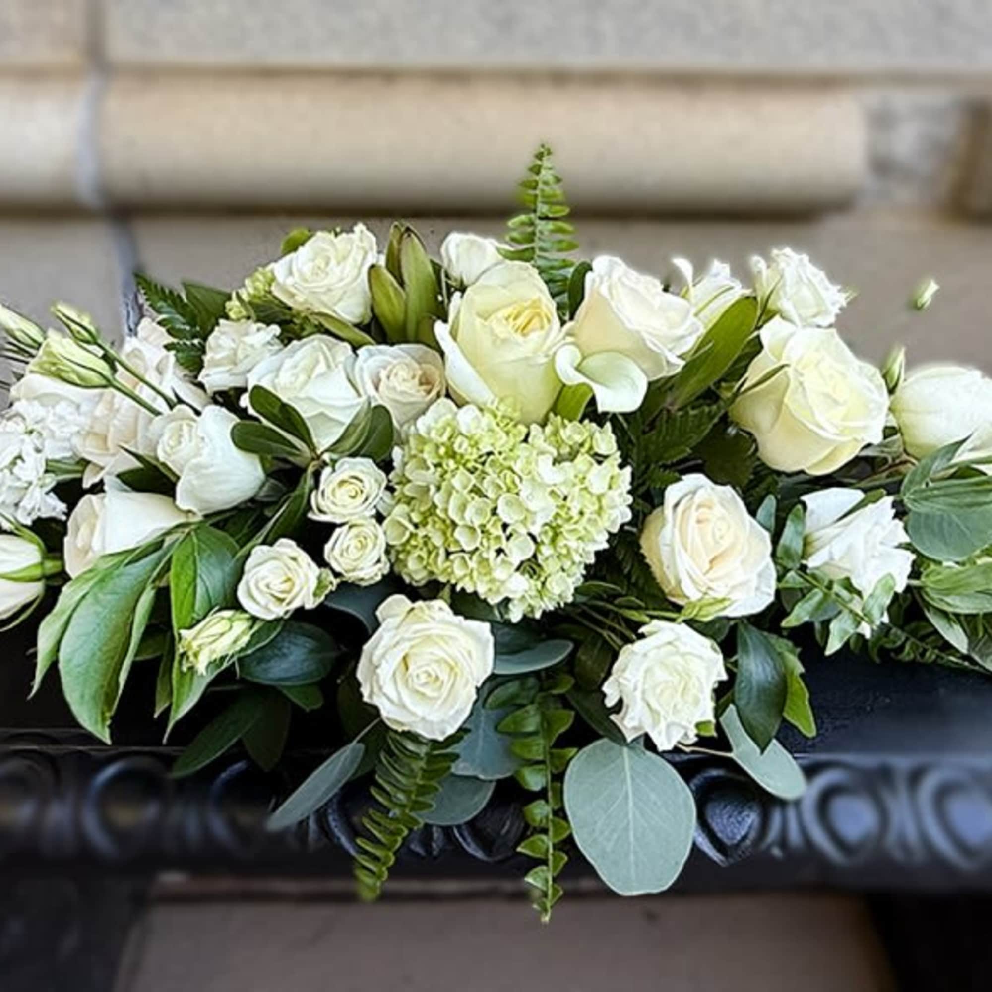 Long low arrangement of white roses and hydrangea with greenery on a dark surface