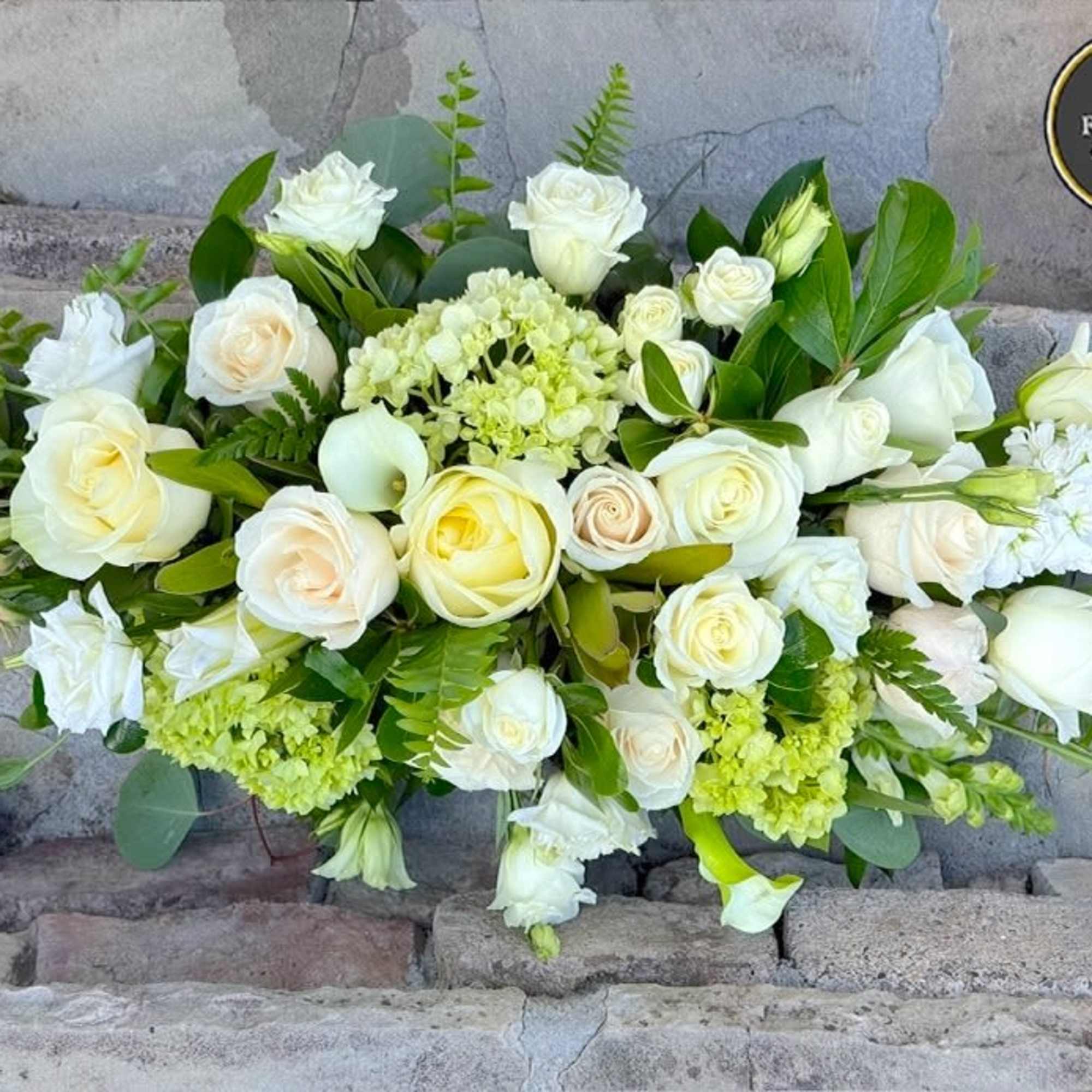 Low arrangement of white and cream roses with soft green blooms in an elongated design