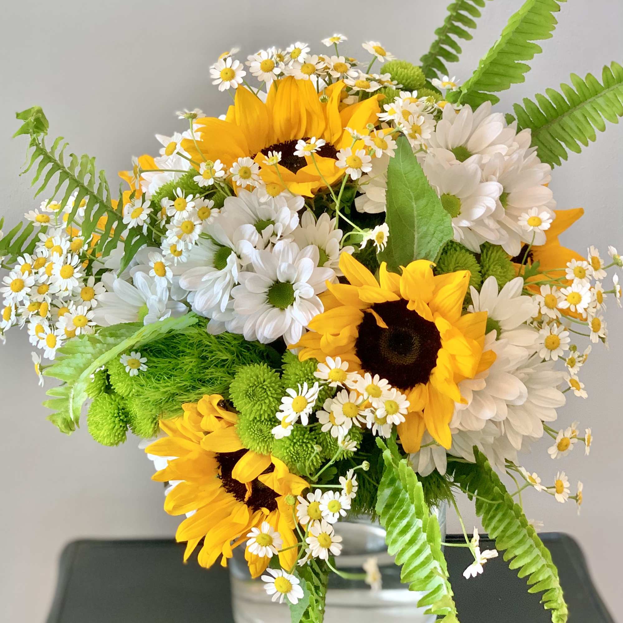 Bouquet of sunflowers, white daisies, and green mums in a glass vase