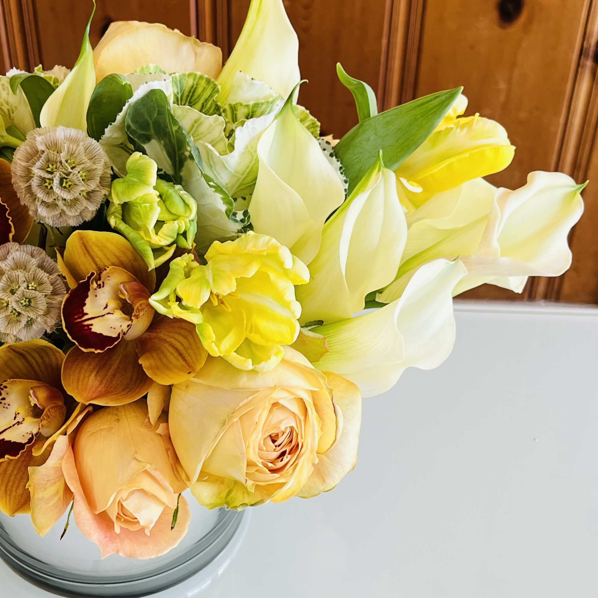 Bouquet of white calla lilies, peach roses, and yellow blooms in a glass vase