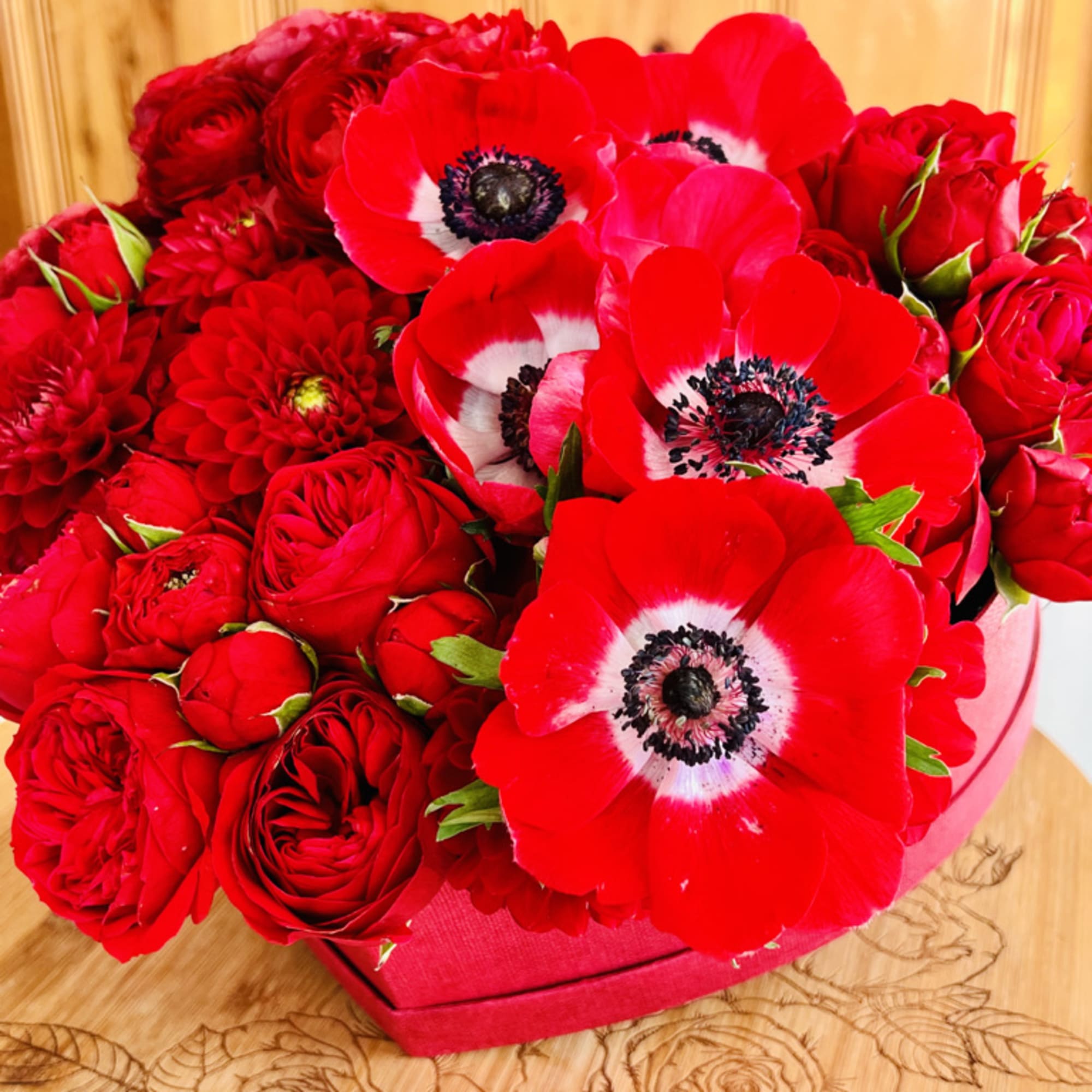 Red roses and red anemones in a pink box