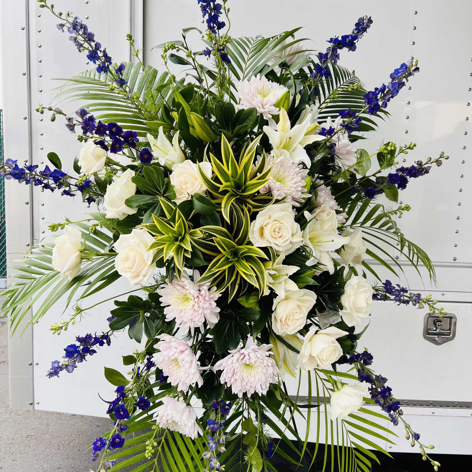 Tall standing floral spray with white roses, lilies, and blue delphinium