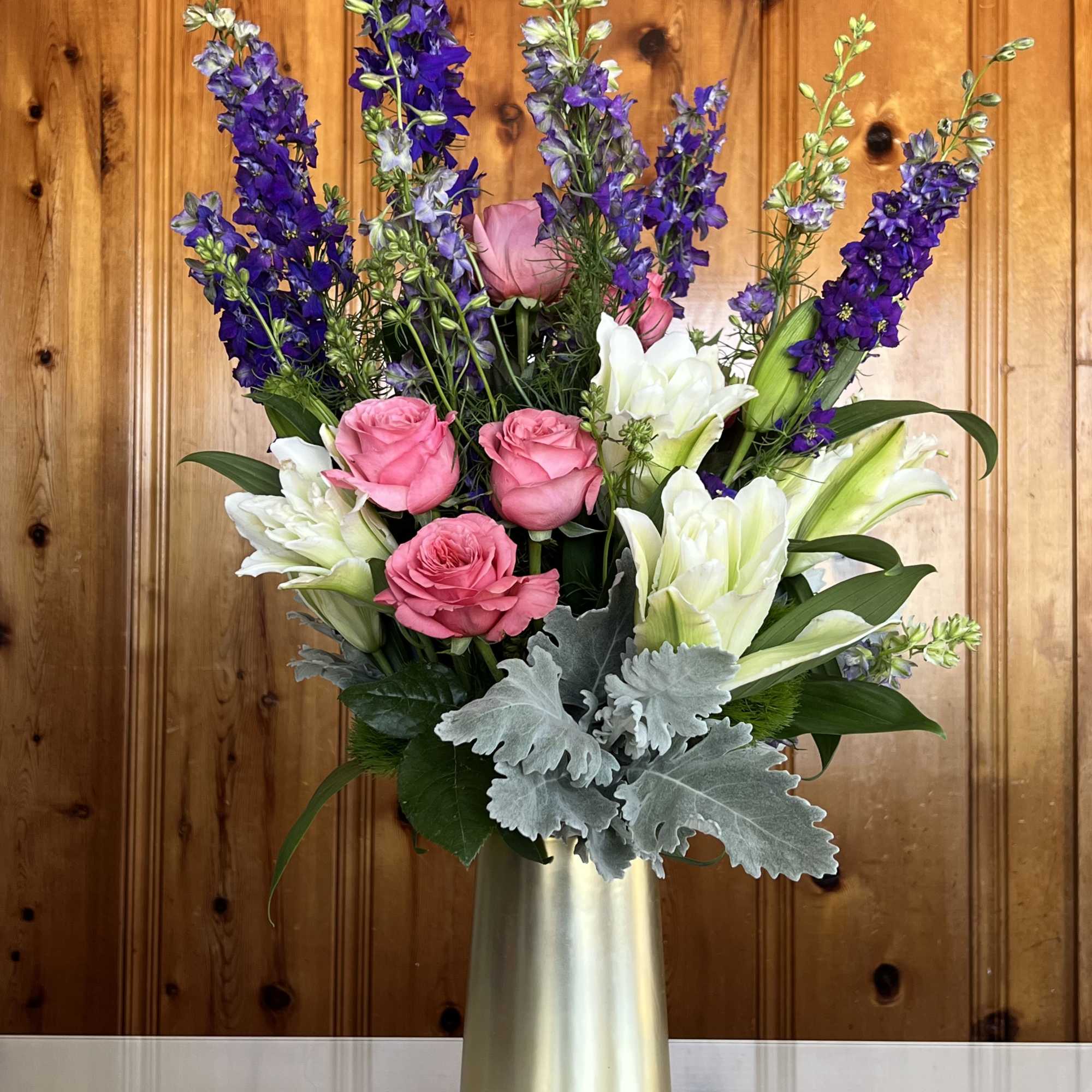 Pink roses and white lilies in a gold vase with tall purple spikes
